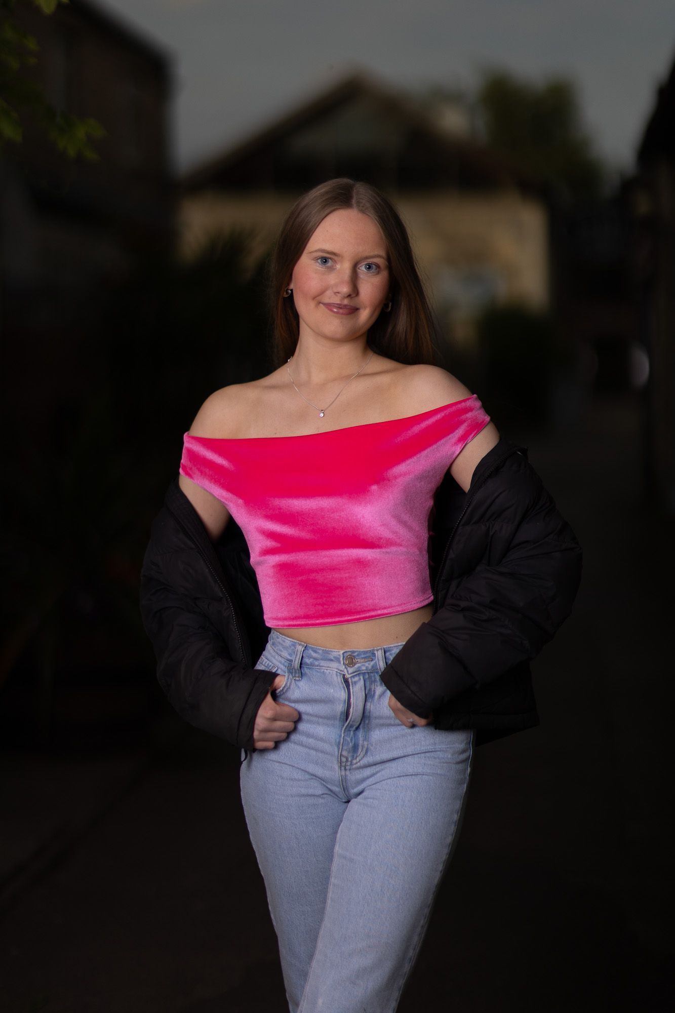 Evening photoshoot featuring pink top, denim and black jacket in urban setting.