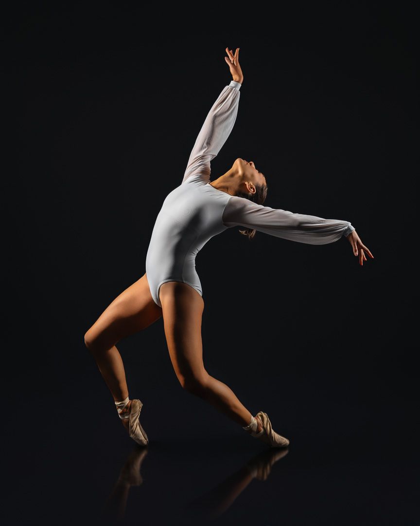 A graceful ballet dancer in a white leotard and pointe shoes strikes an elegant pose against a dark background.