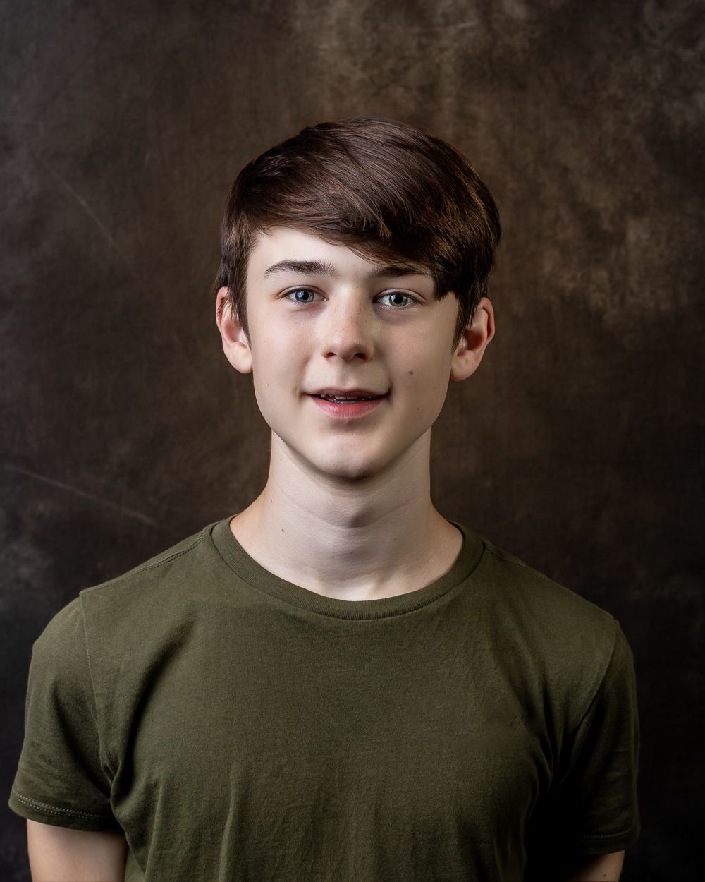 Professional portrait of person in olive green t-shirt against textured background.