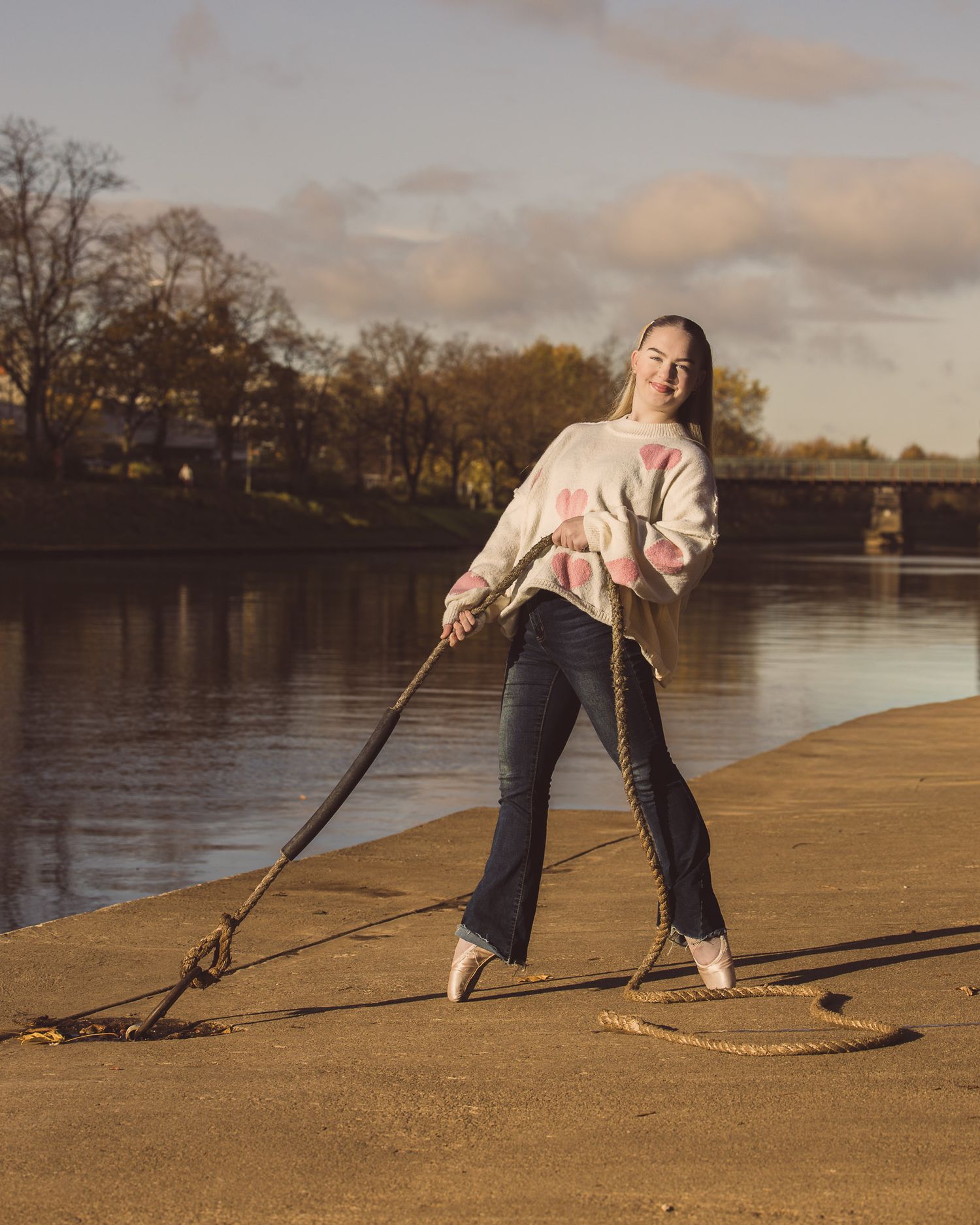 Person pulling on a rope at sunset on a sandy beach beside a calm lake.