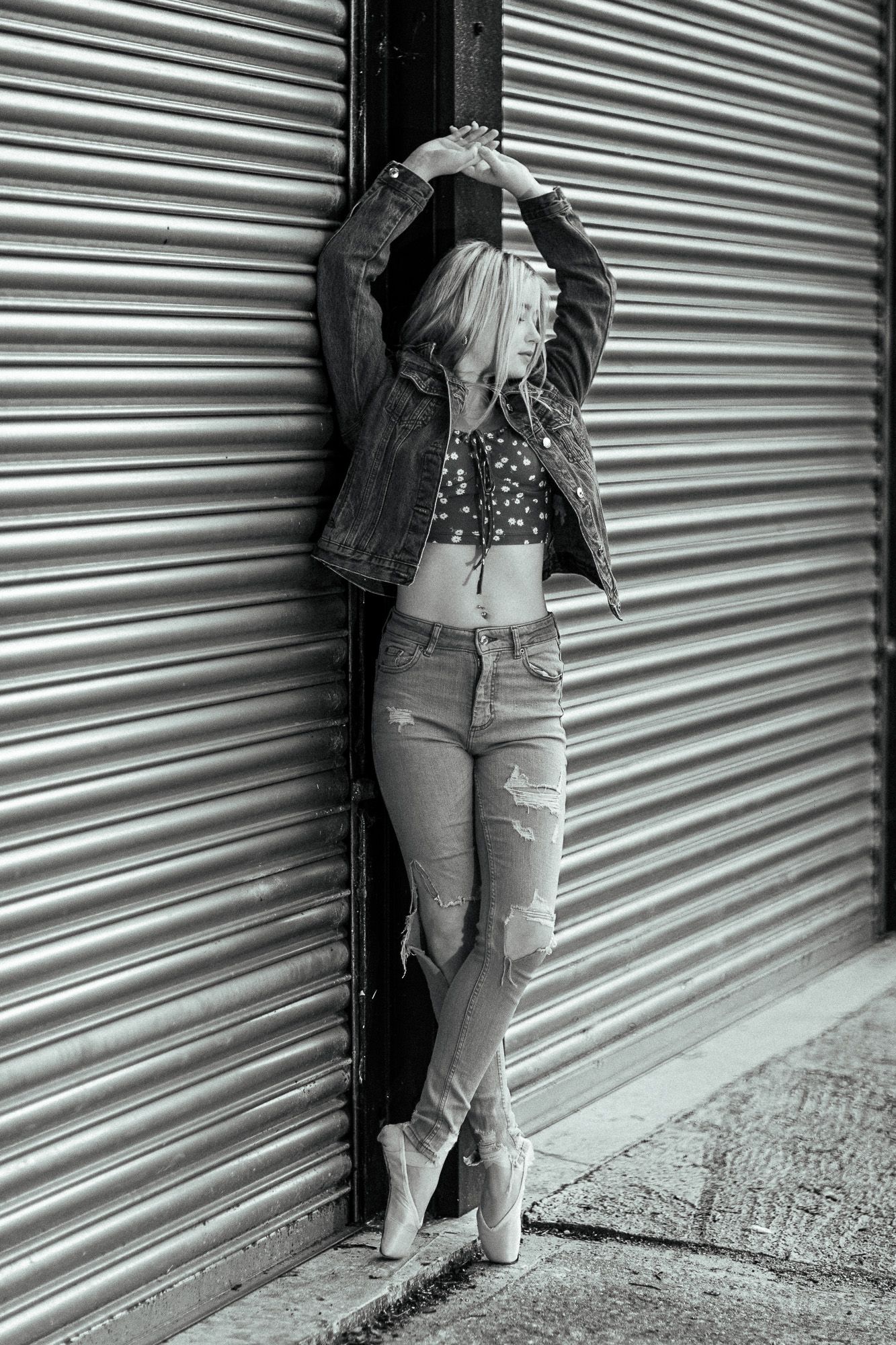 A black and white photo series showing a person posing against metal shutters wearing jeans and a crop top.