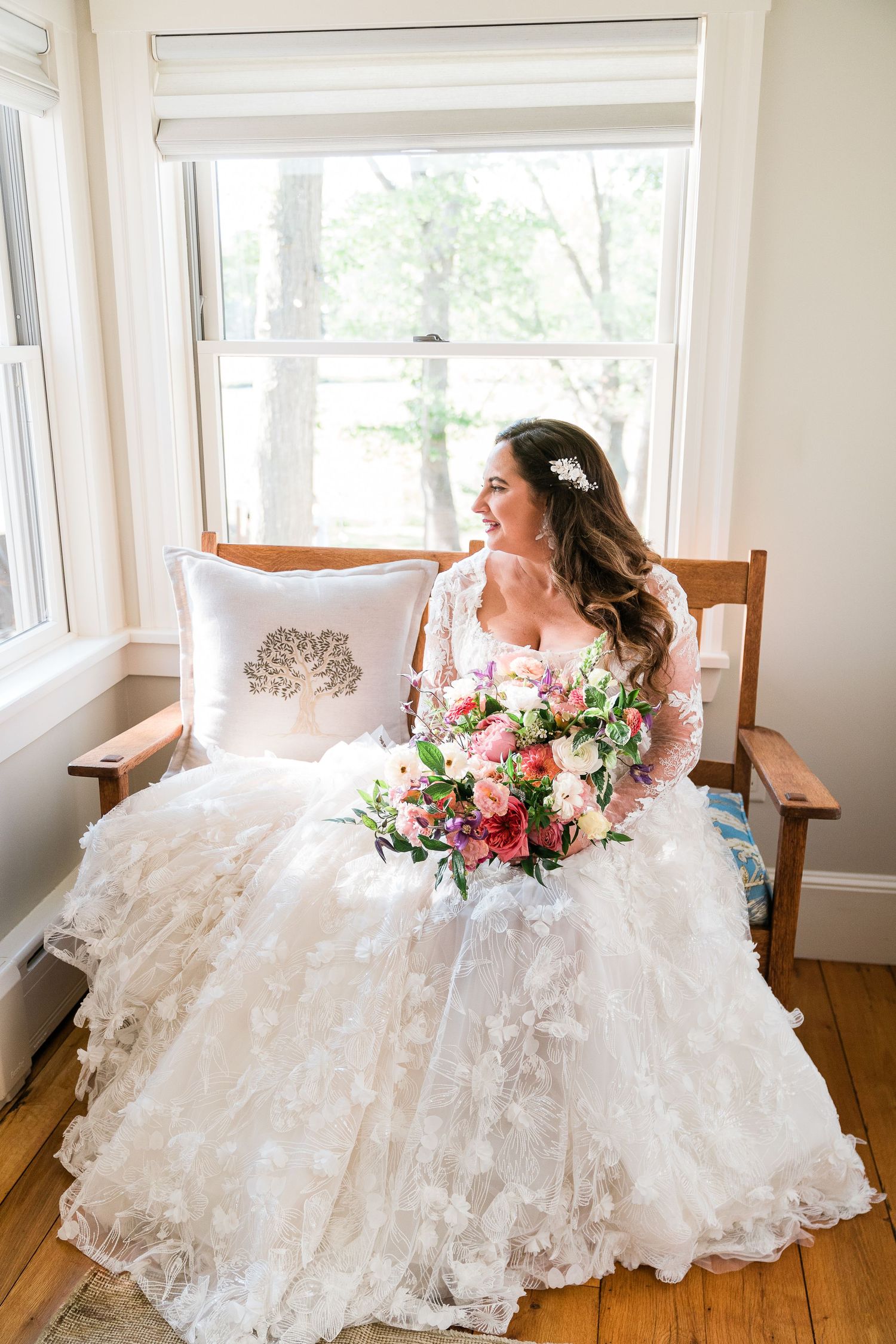 A bride looks out the window holding her bouquet getting ready in her childhood home.