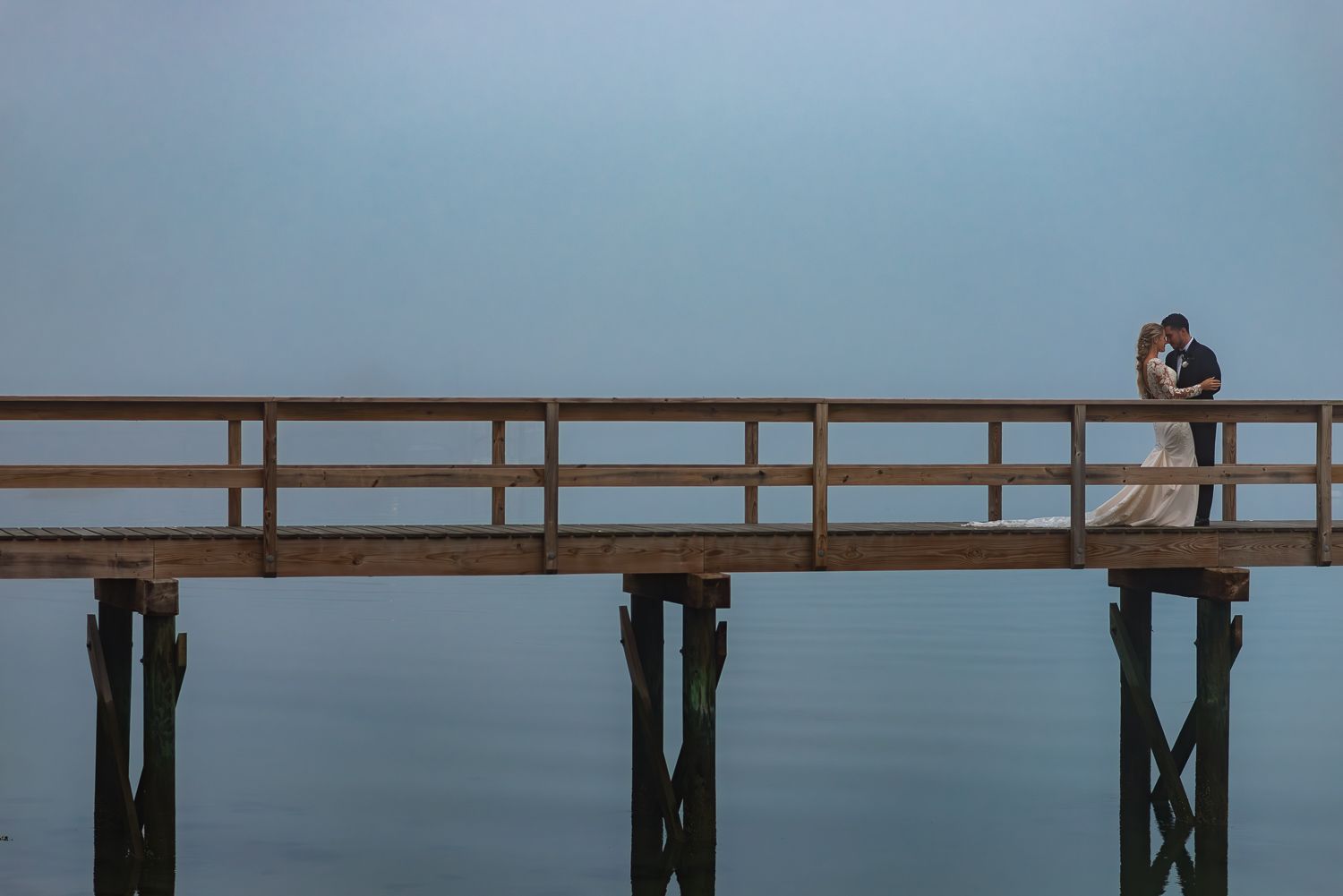 A bride and groom put their heads together on a bridge at dusk in Maine.
