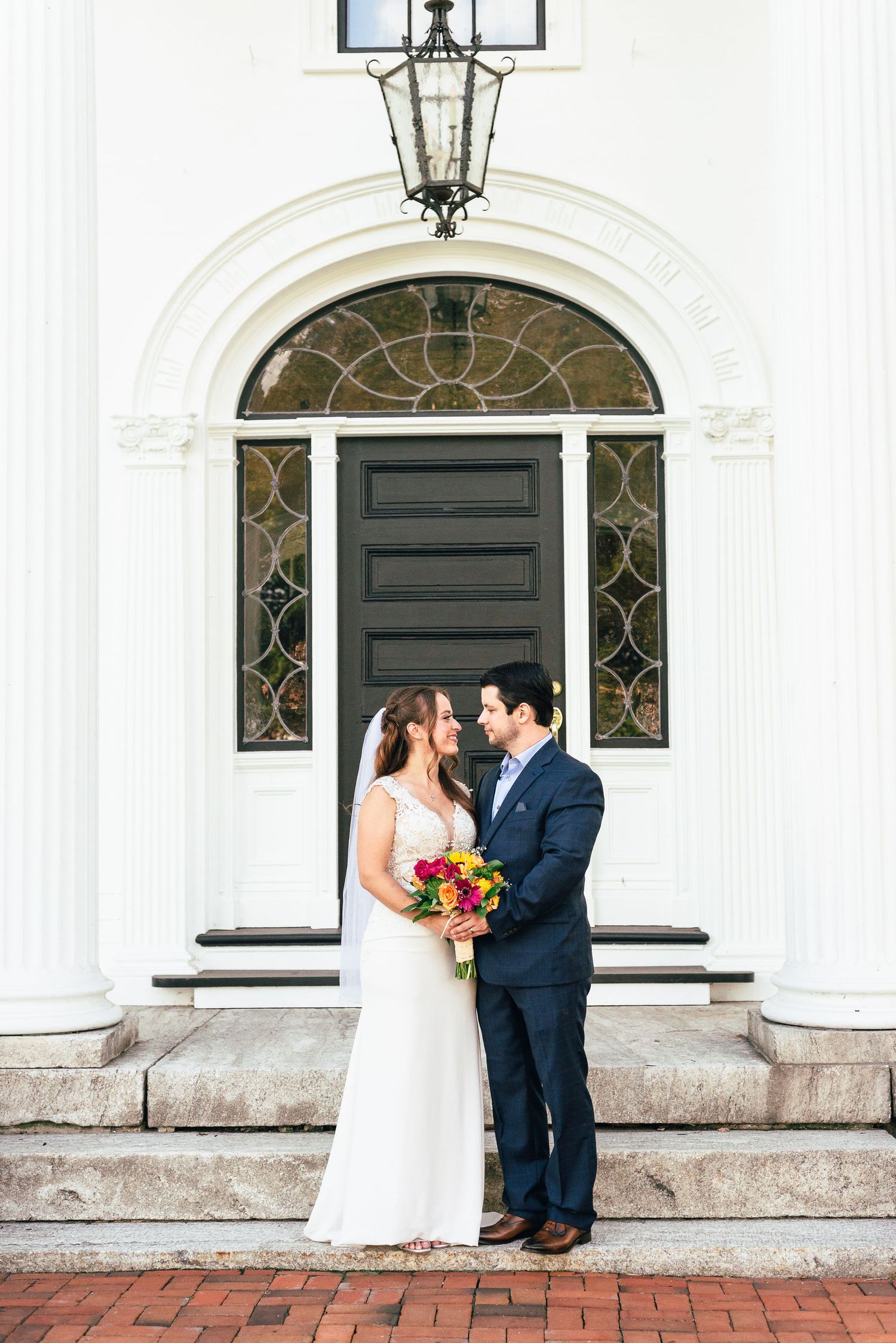 A bride and groom stand in front of an historic building.