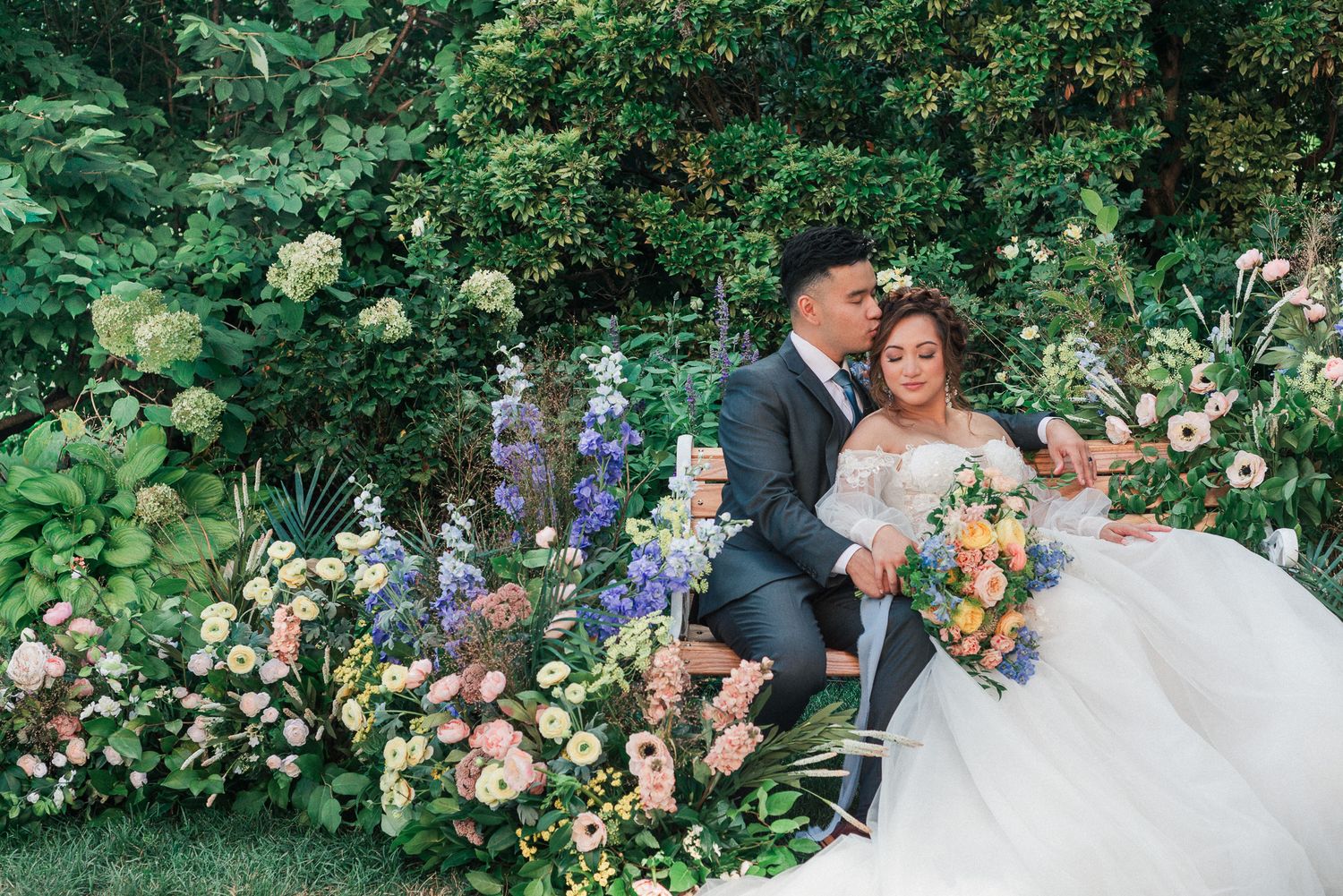 A wedding couple resting on each other surrounded by garden flowers.