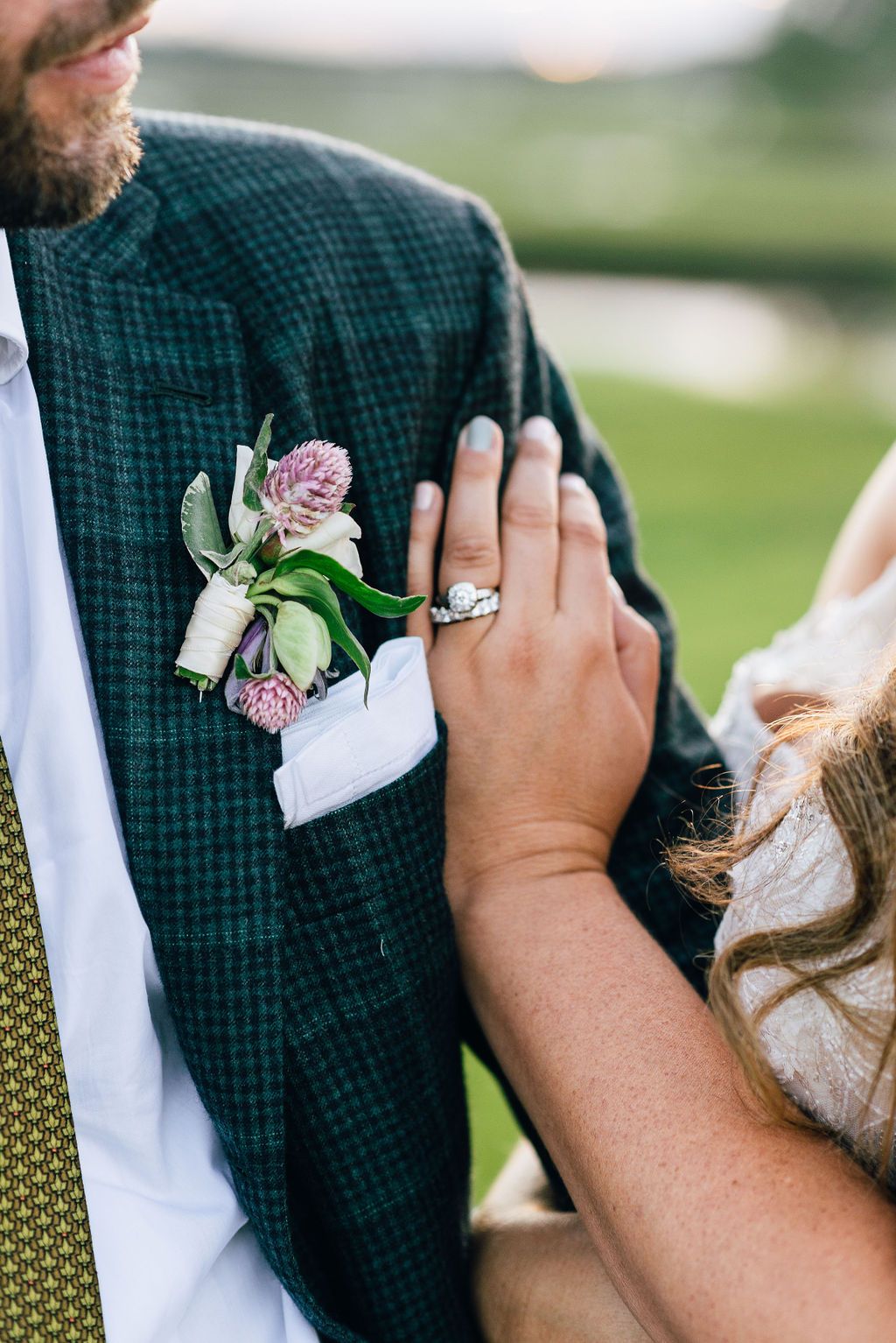 A detail shot of a bride placing her ring hand on her groom to show off the boutonniere.