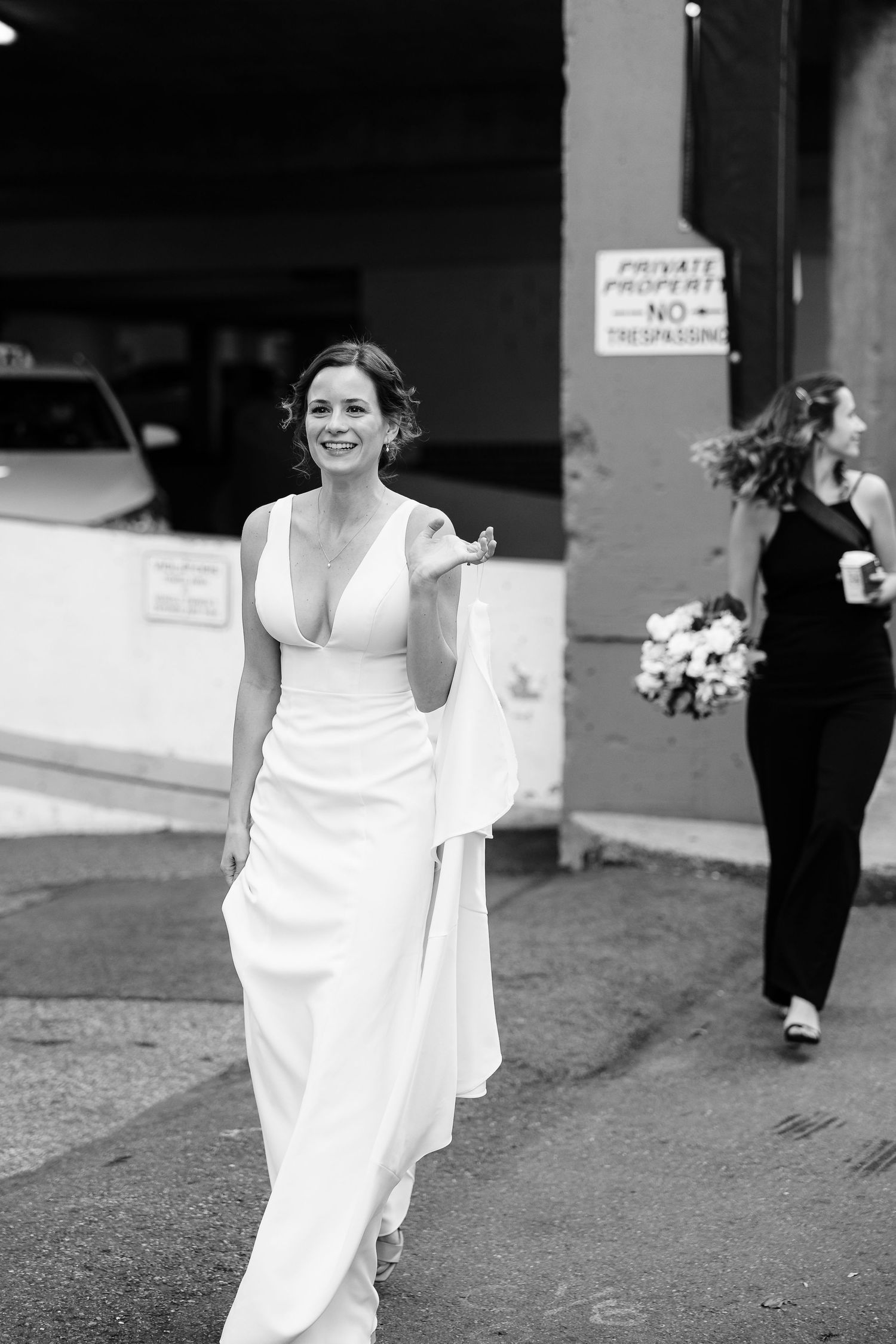 a black and white candid shot of a bride walking down a city street to her wedding, her arm raised so her train doesn't trail on the ground