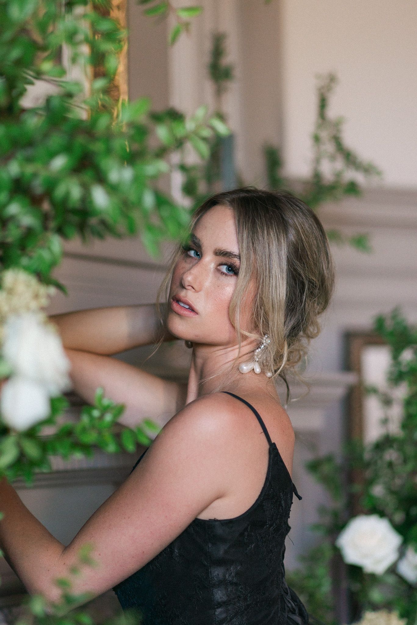 A model poses against a fireplace mantle surrounded by greenery.