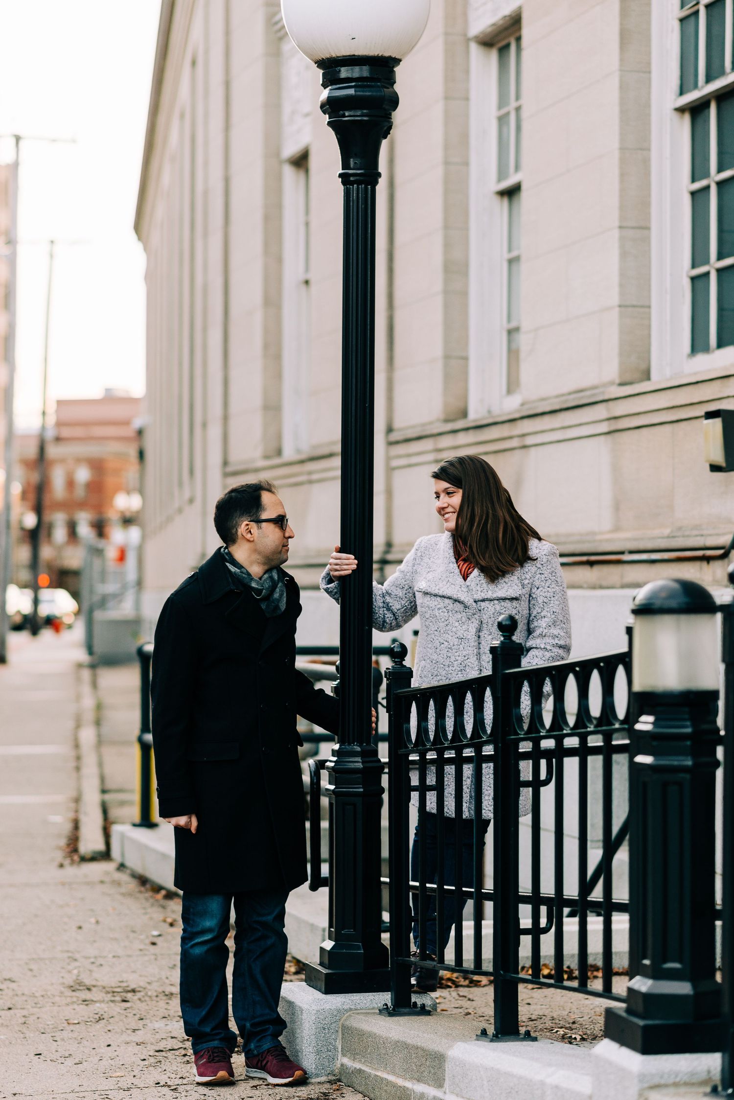 An engagement couple looking at each other next to a lamp in a city.