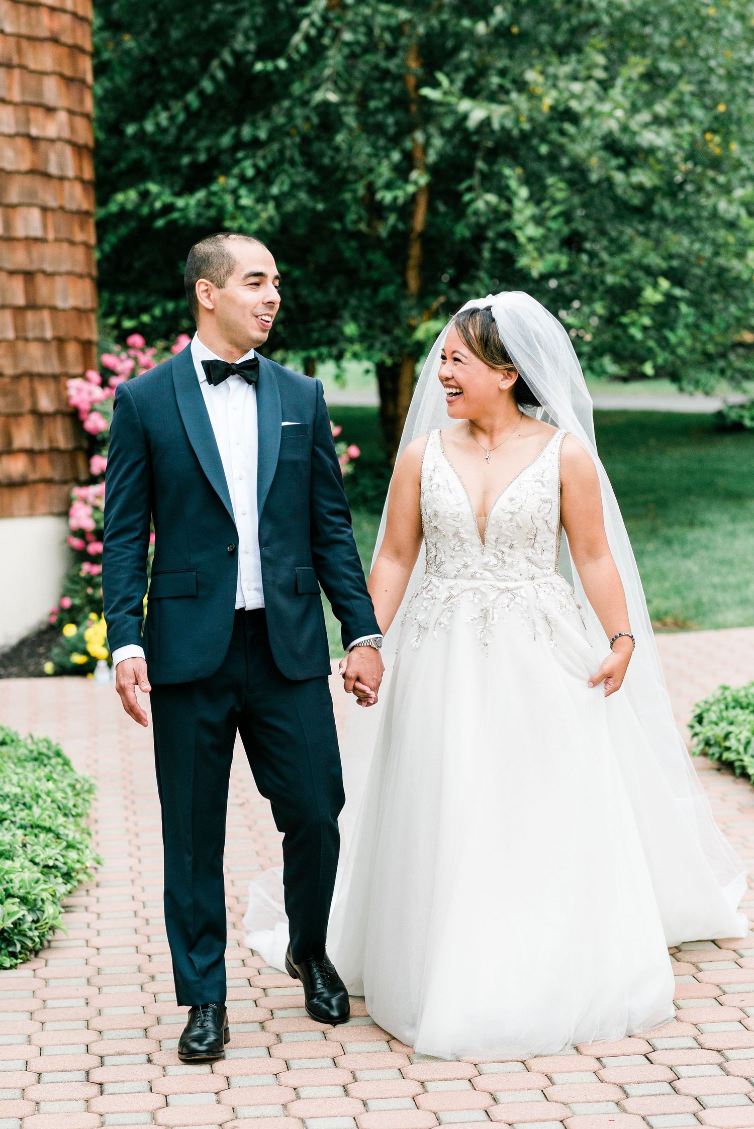 a bride and groom smile at each other as they walk down a brick path
