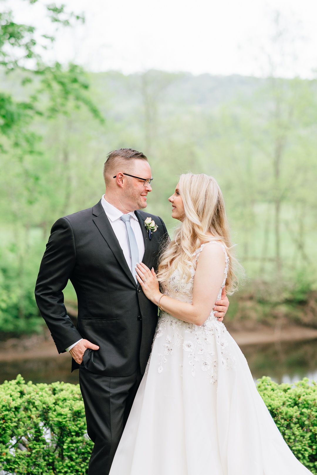 A bride and groom smile at each other surrounded by greenery
