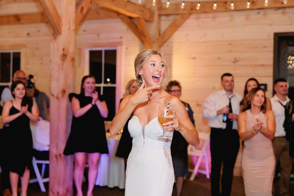 a candid shot of a bride at her barn wedding reception shoots one of her guests a finger gun