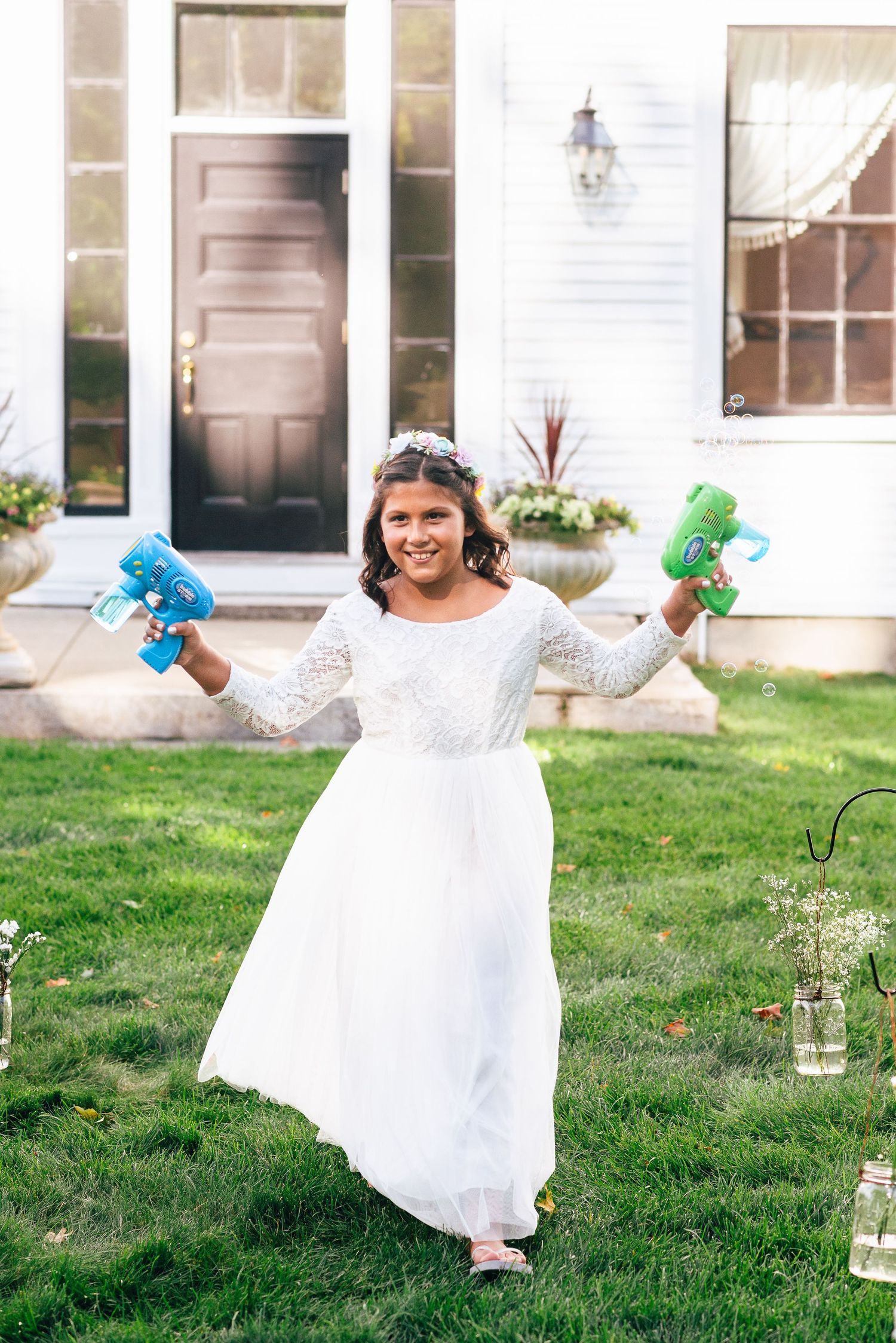 a flower girl walks down the aisle, both hands carrying bubble guns