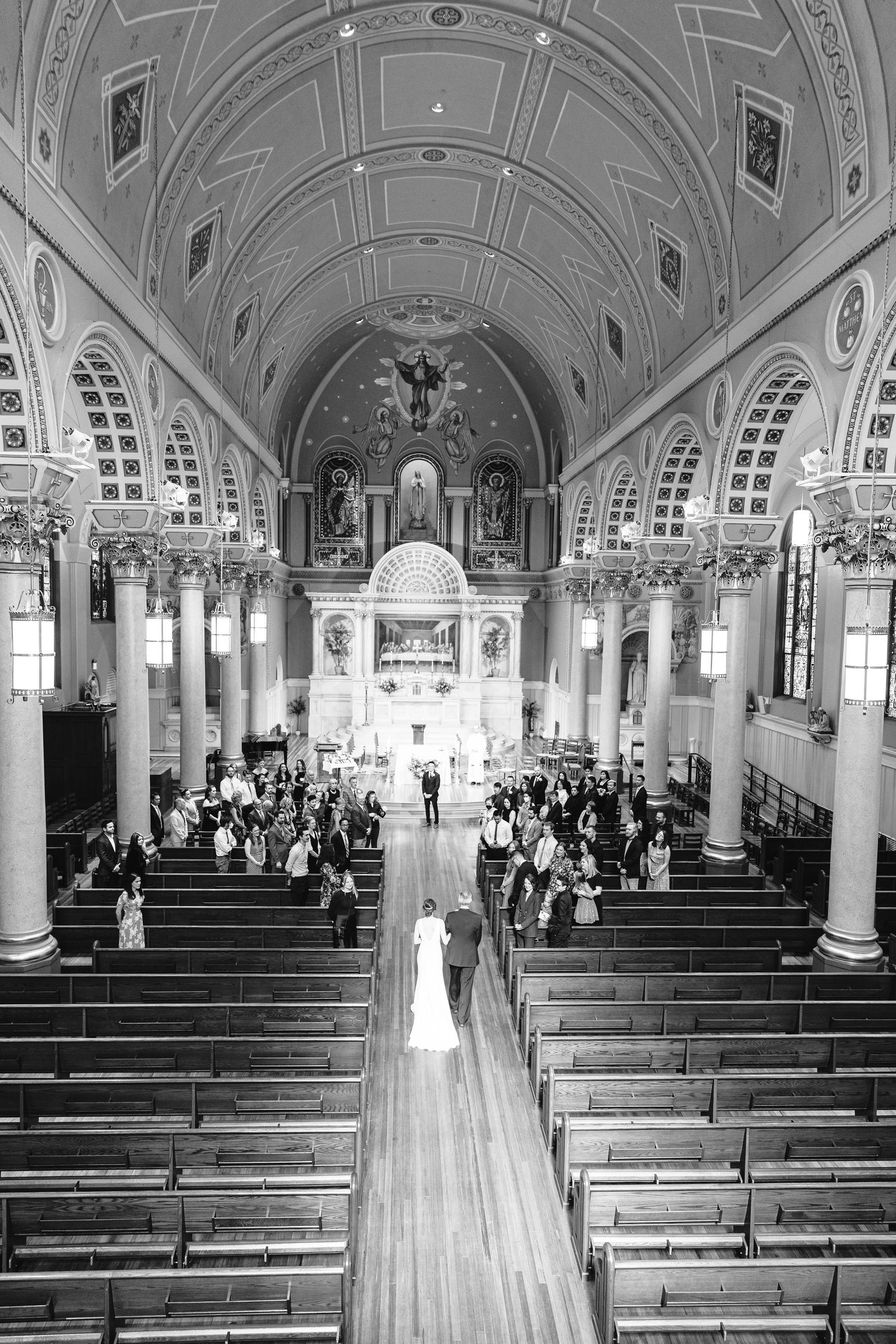 An overhead black and white shot of a bride walking down the aisle in a church ceremony.
