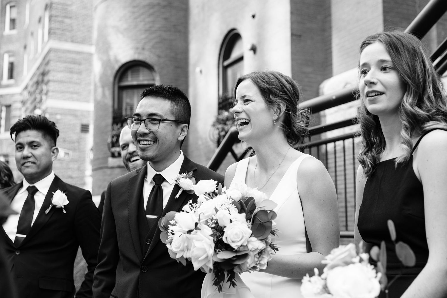 Black and white candid photo of bride and groom laughing with their guests at their wedding ceremony.
