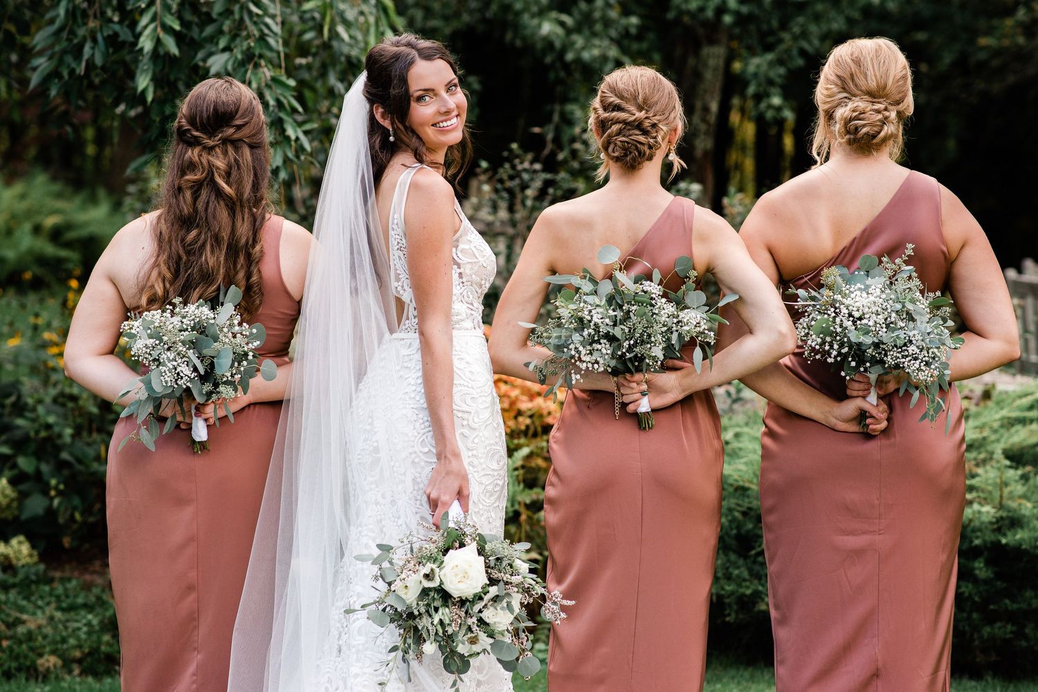 three bridesmaids in pink face away from the camera as the bride faces the camera and smiles