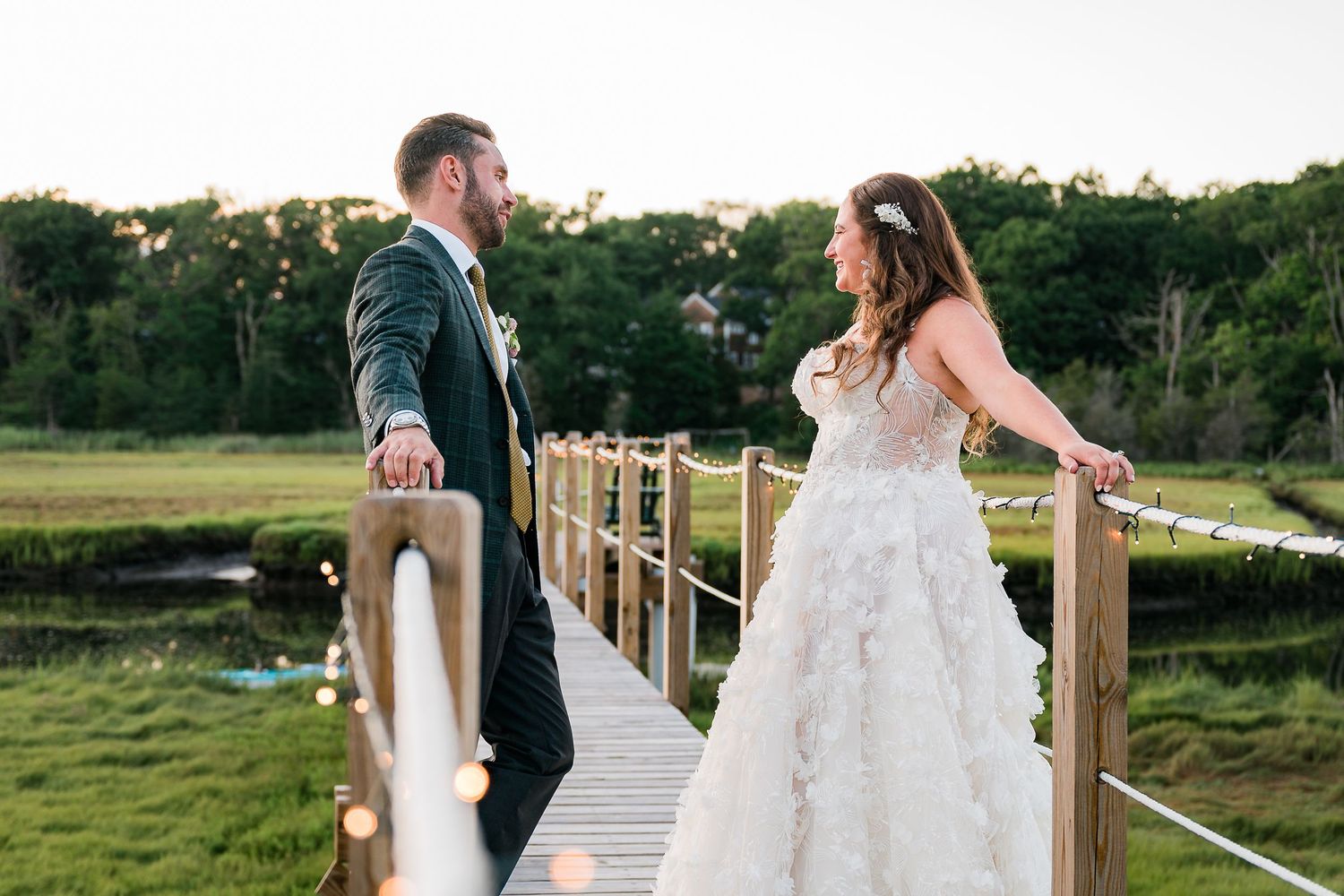 a bride and groom look and smile at each other on a pier