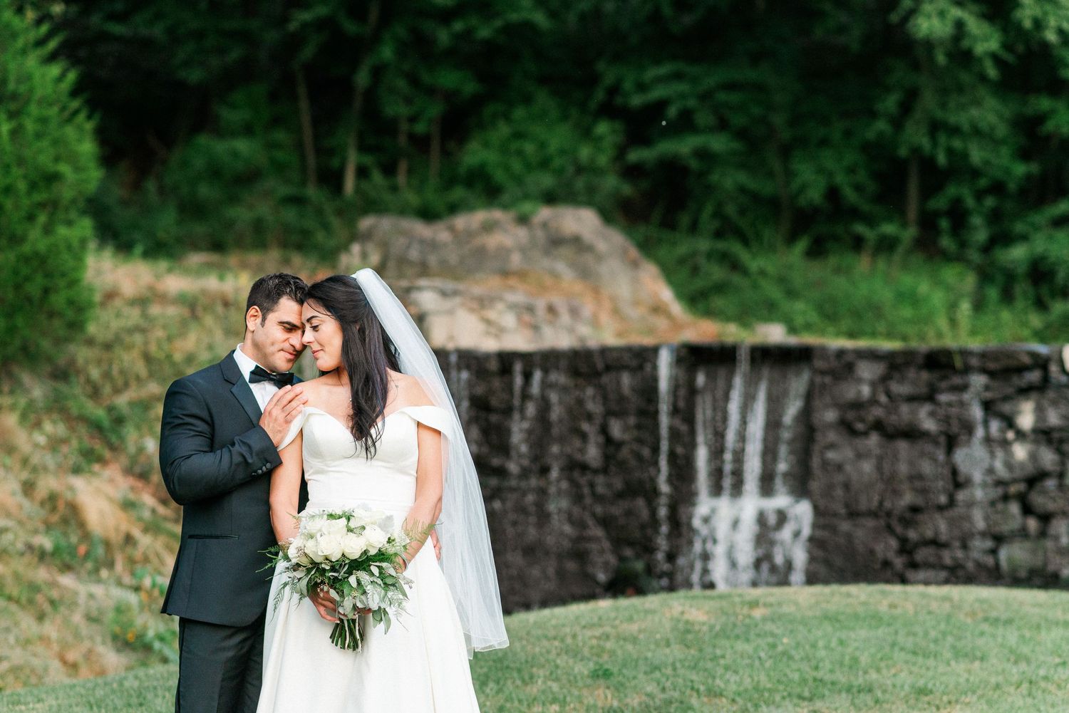 a bride and groom rest on each other as they stand in front of a golf course waterfall