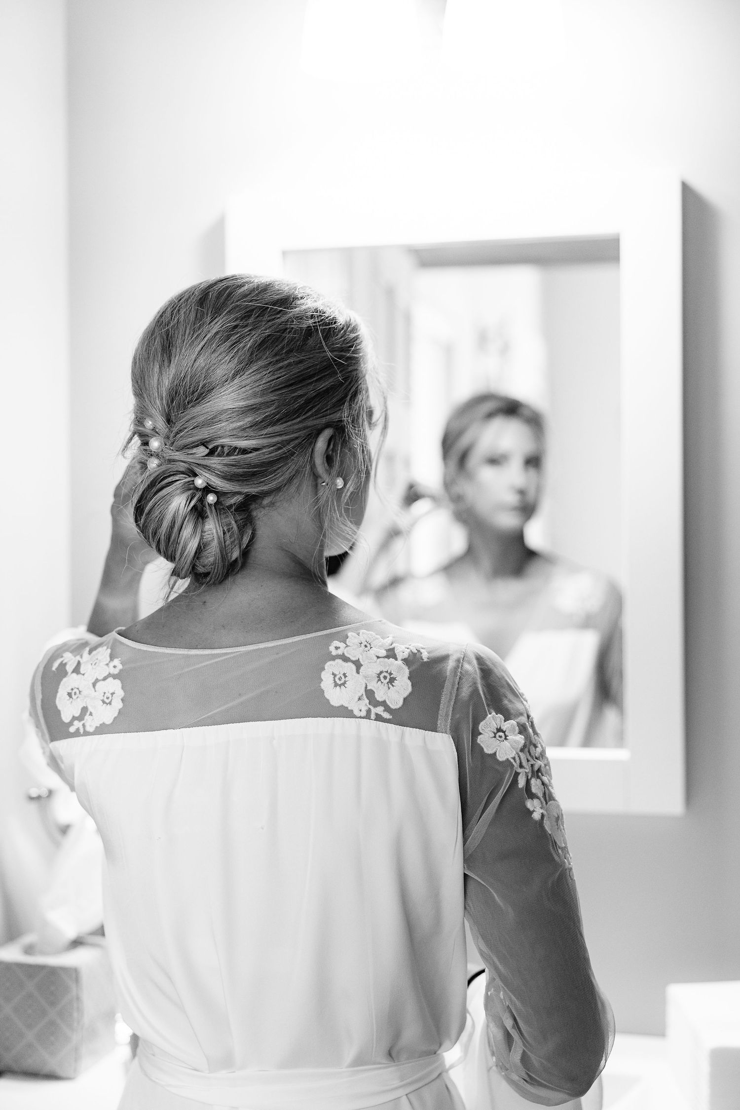 a black and white candid photo of a bride getting ready for her wedding in the mirror