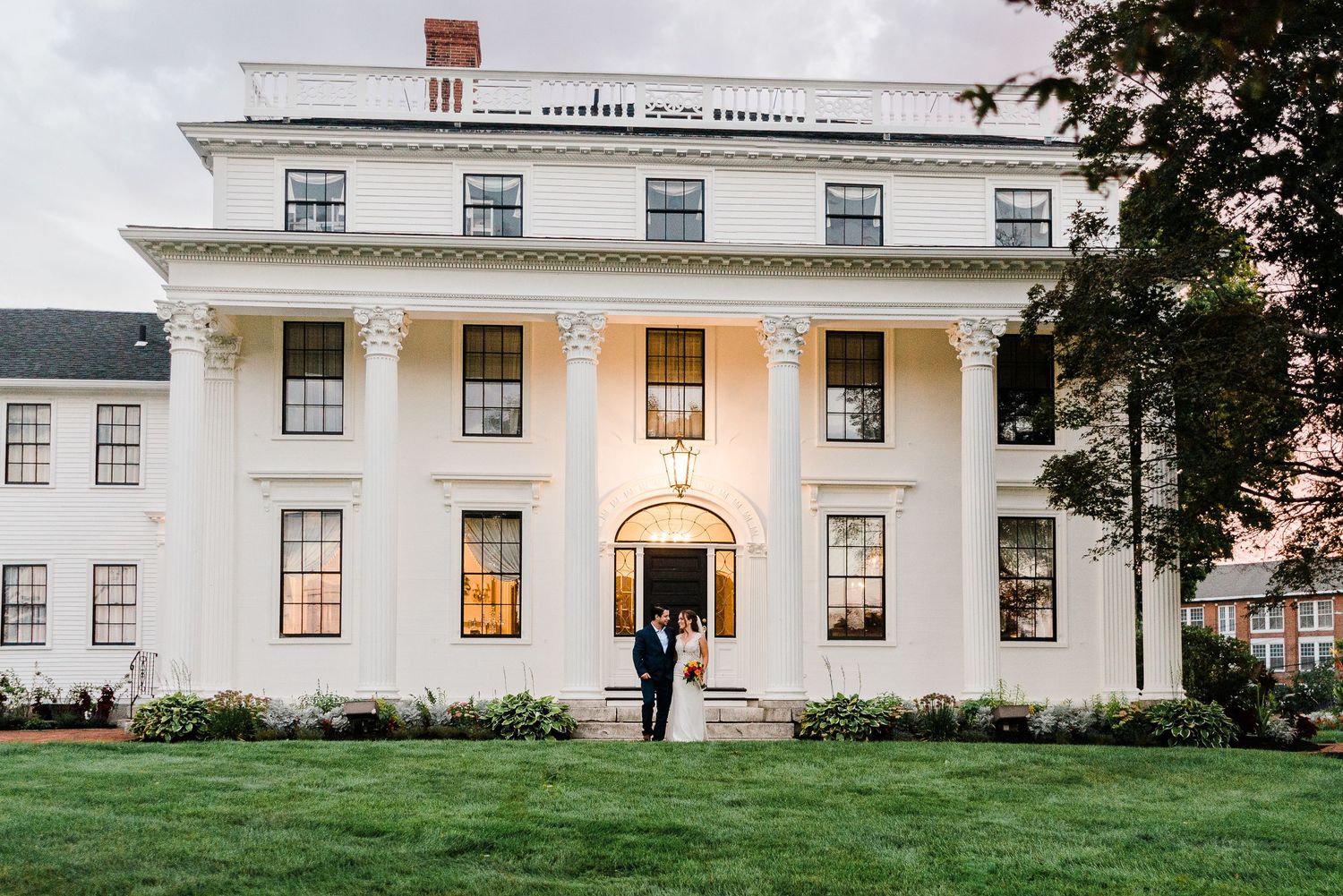 a bride and groom pose in front of an historic home