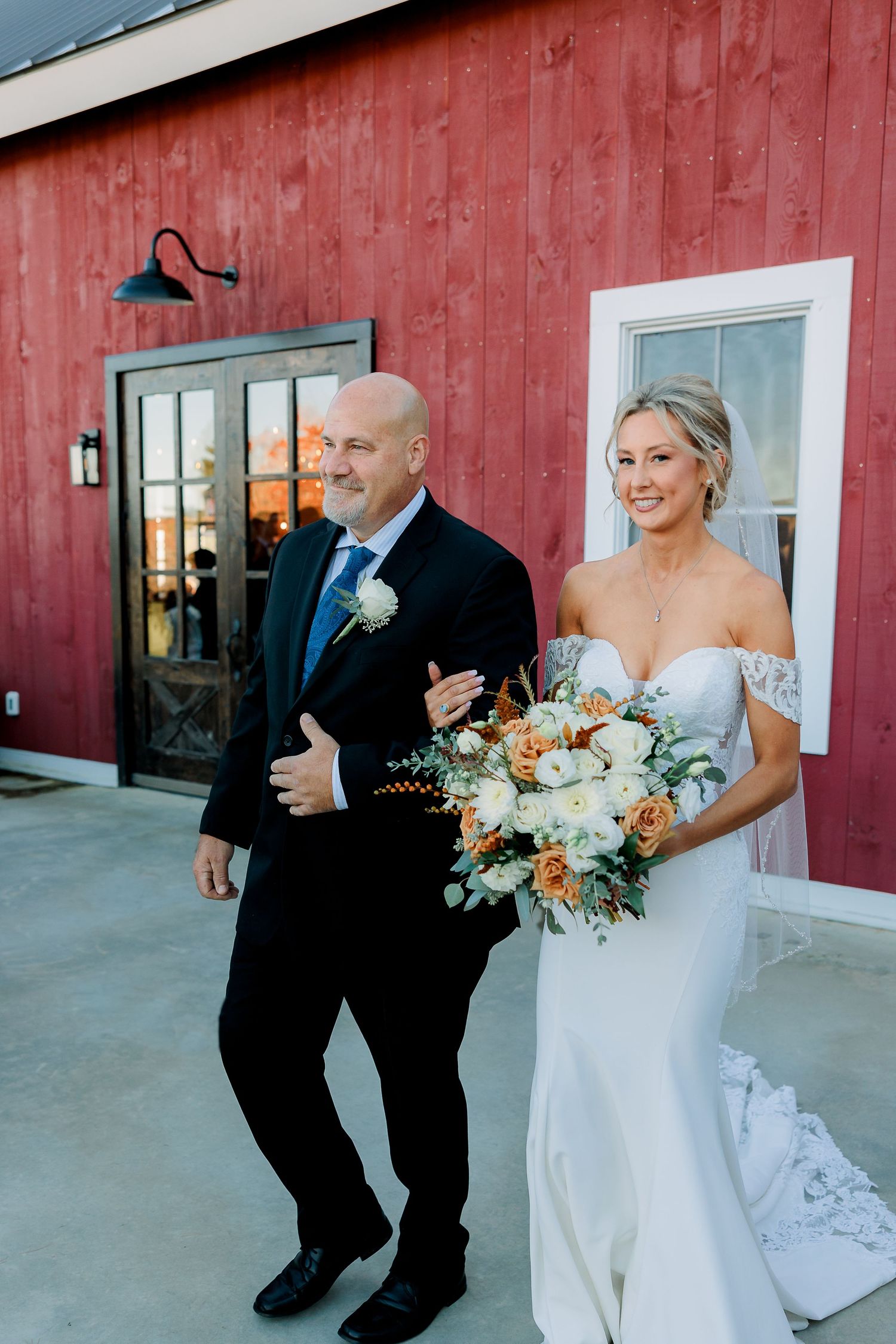 a father walks his daughter down the aisle outside of a red barn