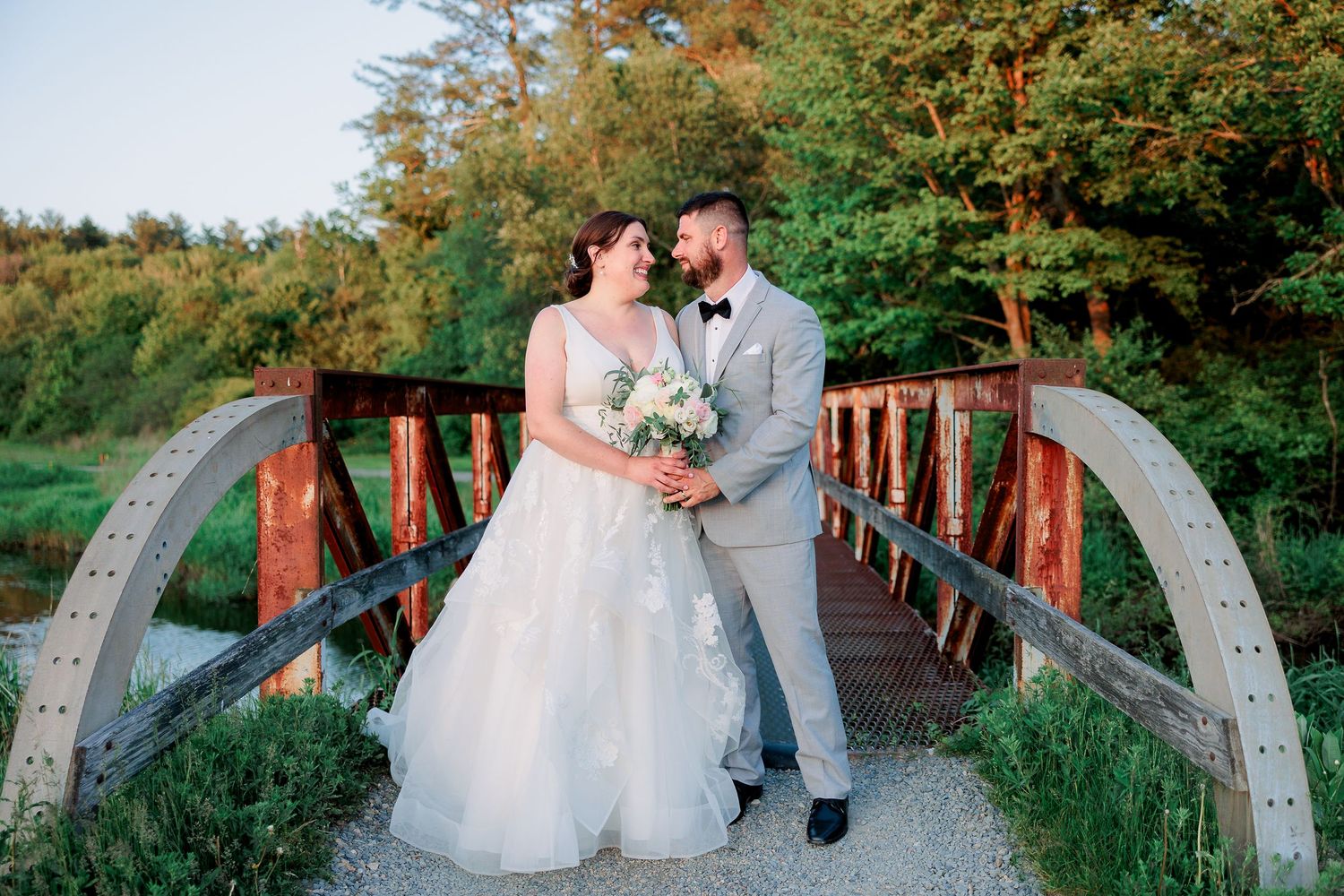 a bride and groom stand on a bridge and smile