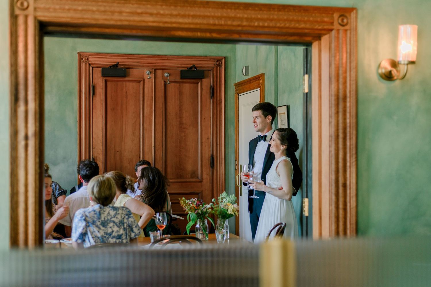 A bride and groom look at their guests in a candid shot, framed by the door.