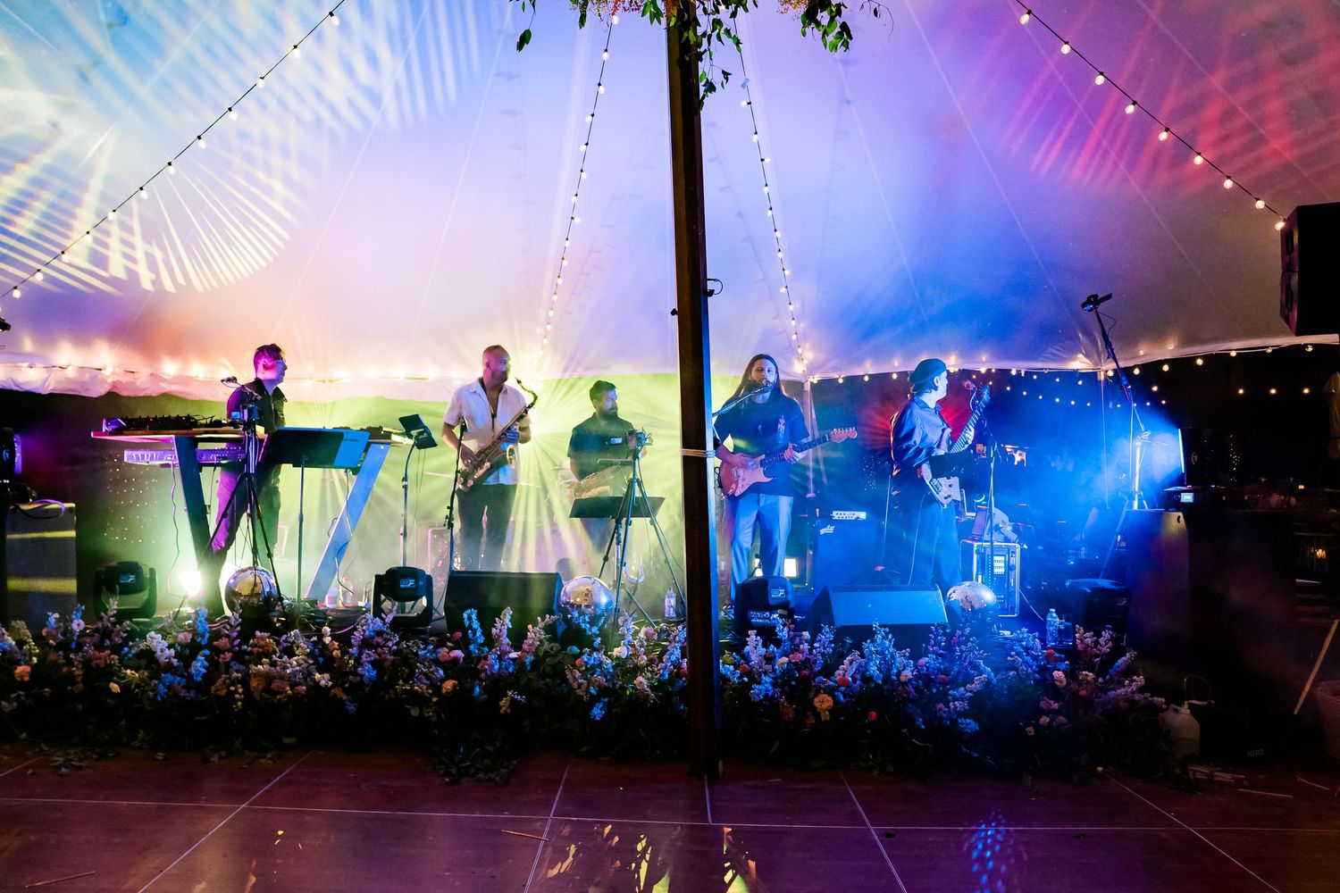 a full band plays at a wedding reception with rainbow lights as a backdrop