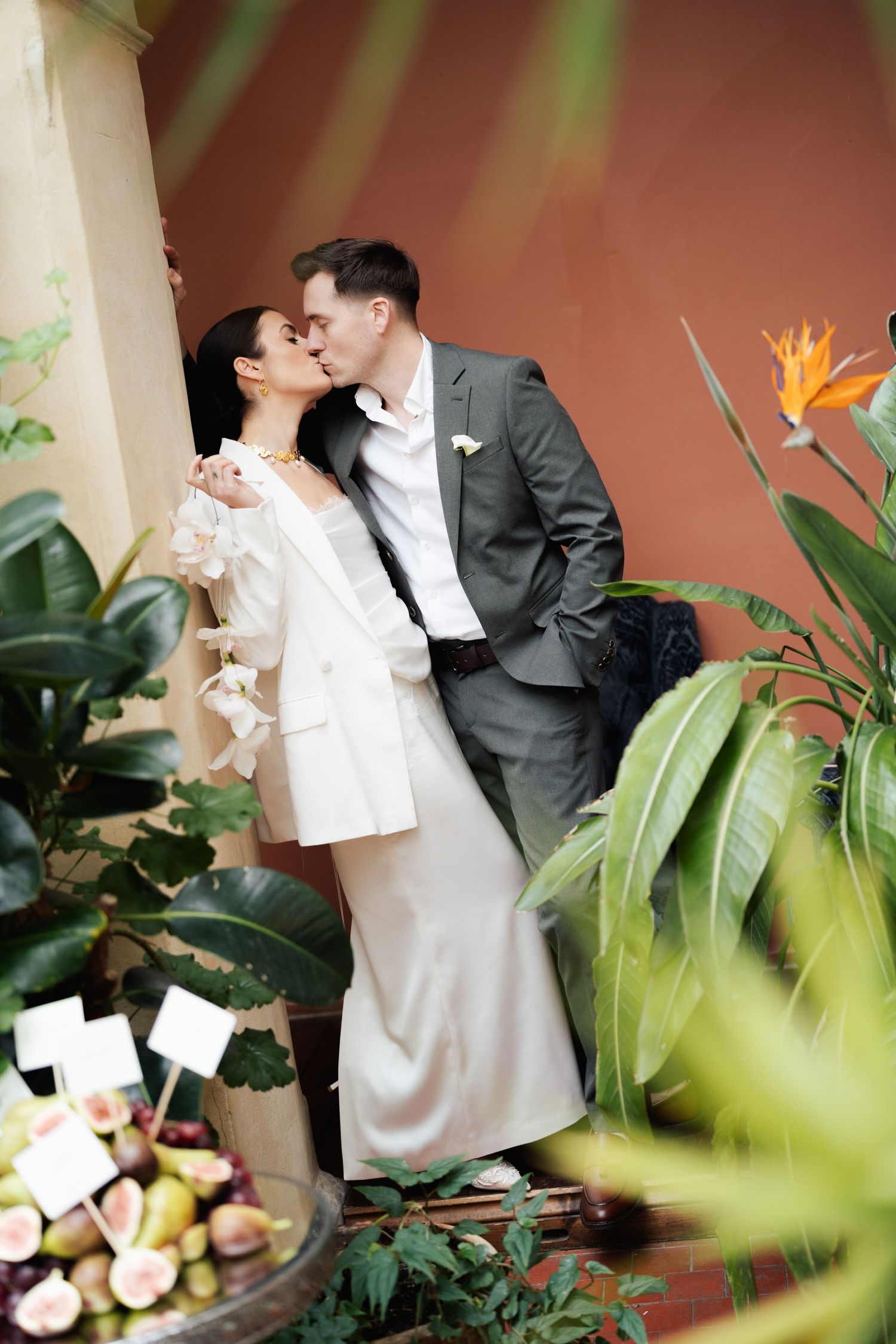 Romantic wedding couple shares intimate moments in a tropical garden setting with lush green plants and coral walls.