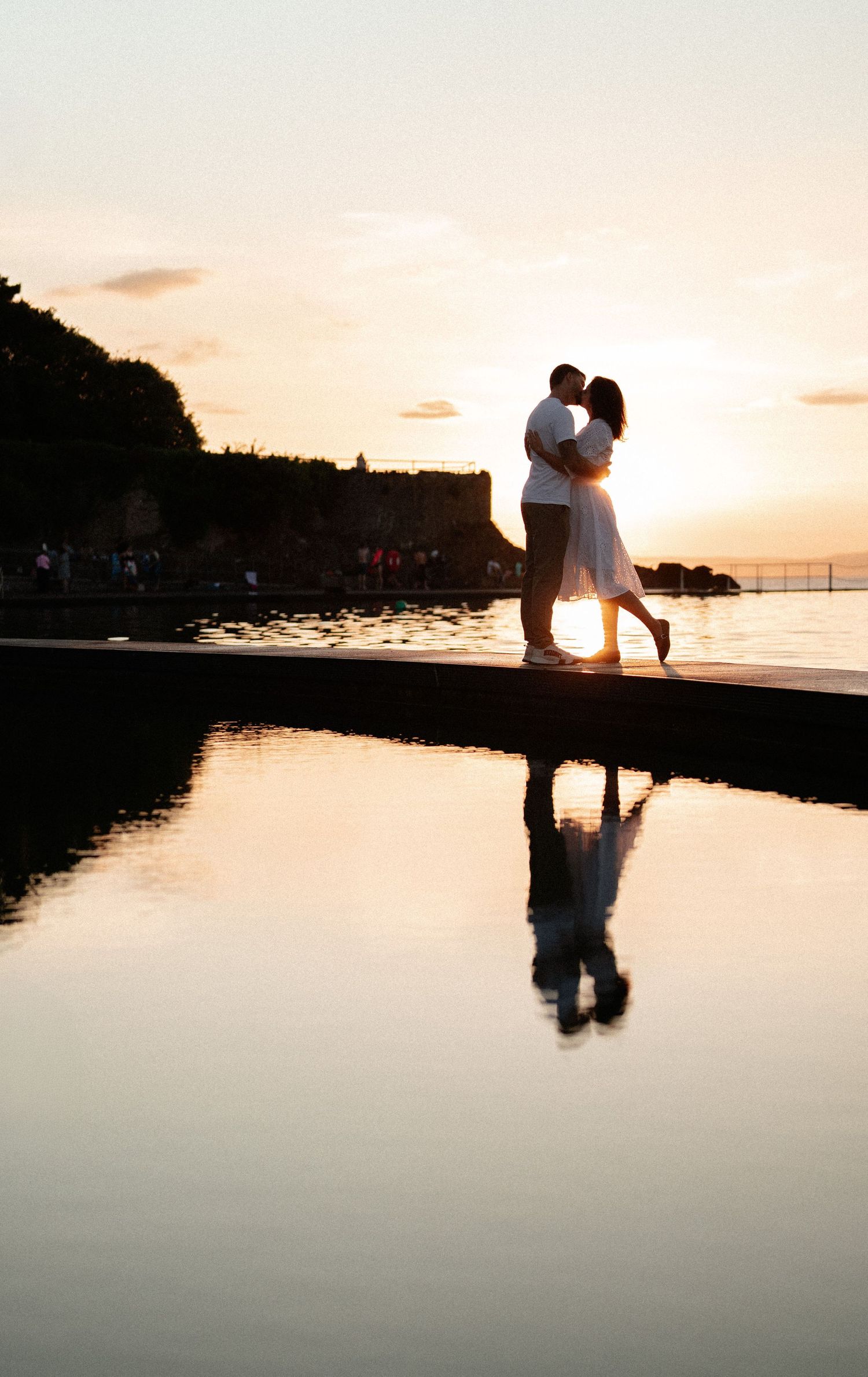Romantic silhouettes reflected in calm water at sunset by the ocean.