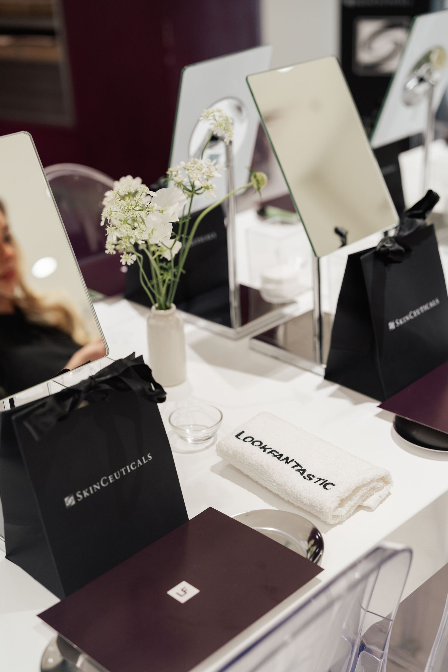 SkinCeuticals black gift bags and mirrors on a white vanity table with a Lookfantastic tote and white flowers.