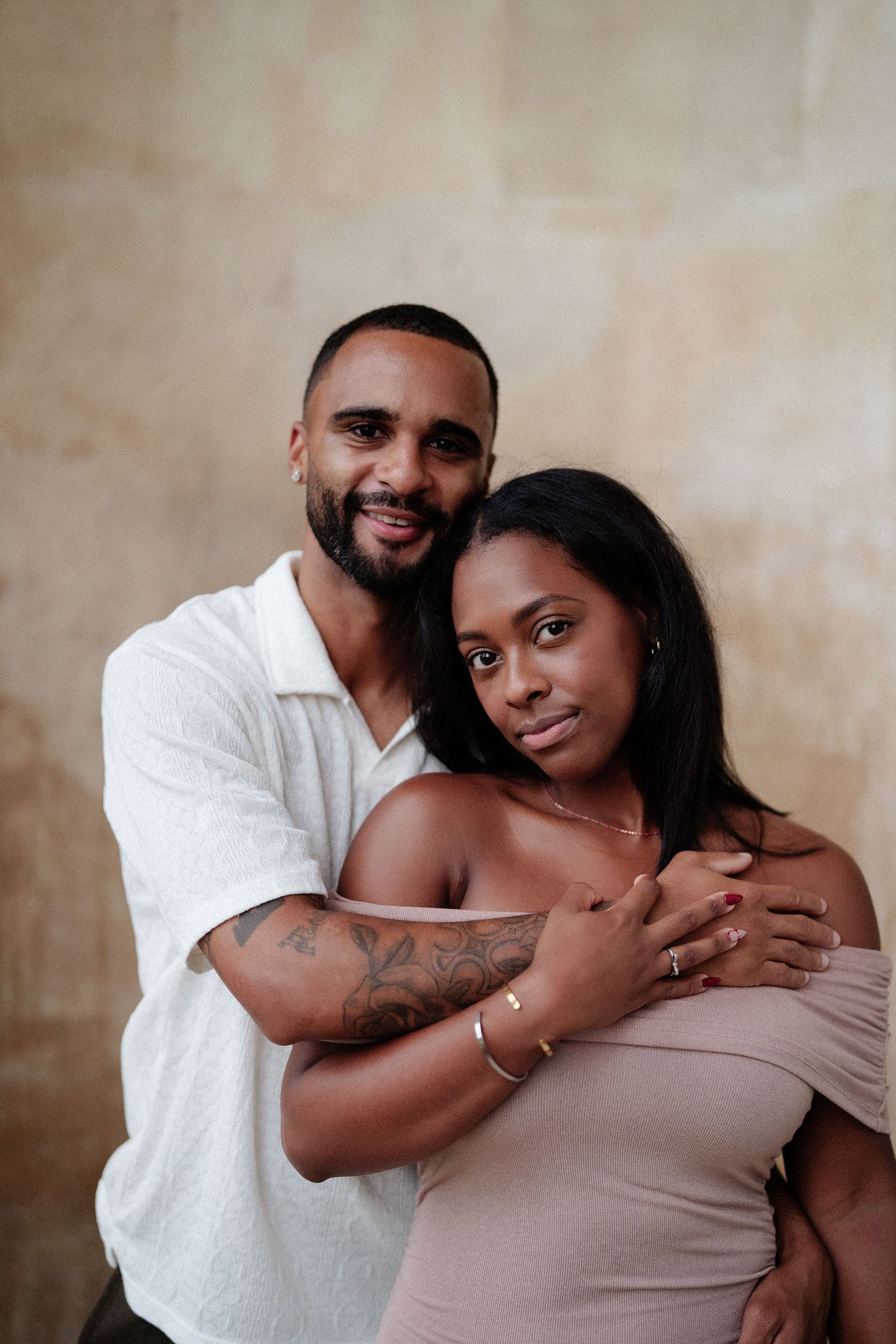 A romantic couple embraces in an intimate portrait against a neutral beige background.