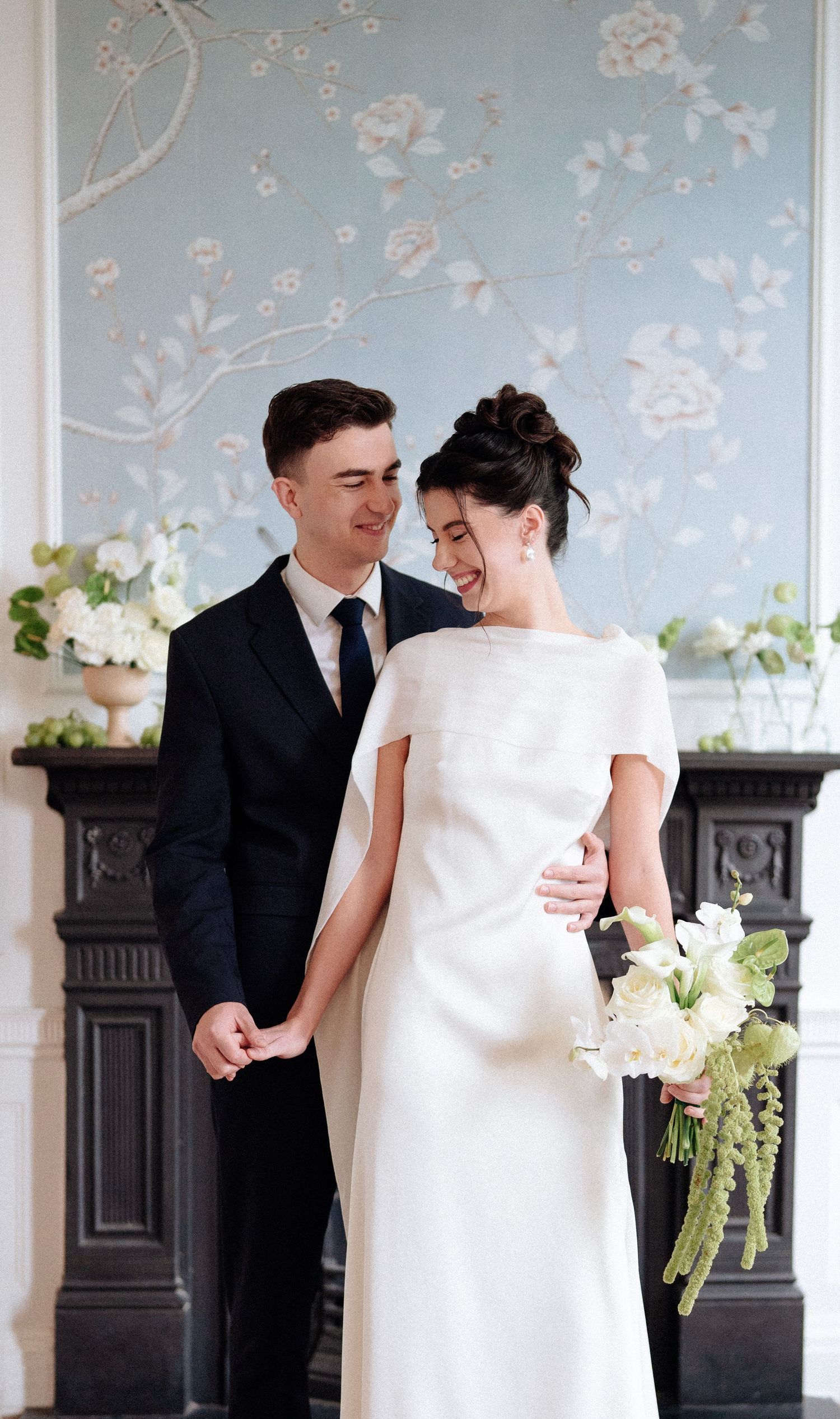 A couple in wedding attire shares intimate moments against a light blue floral wallpaper background.