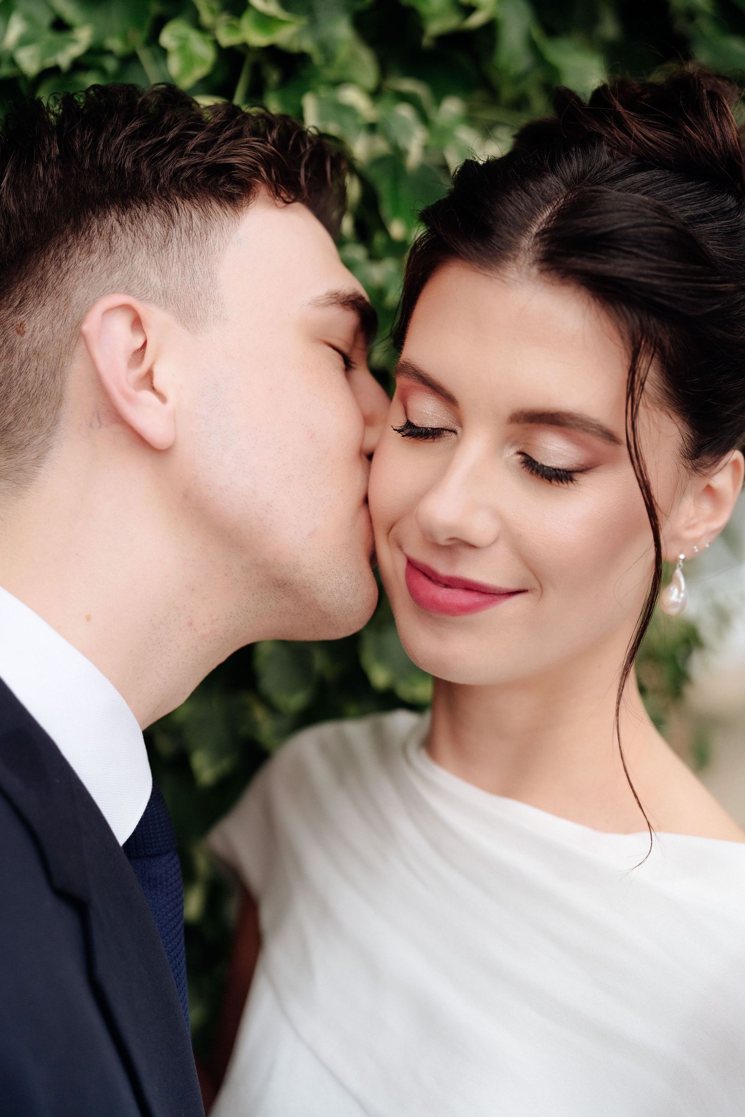 Romantic close-up wedding photos showing tender moments between newlyweds against a green leafy backdrop.