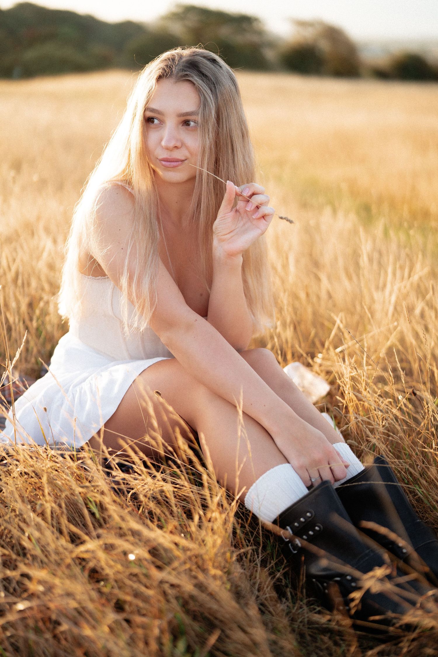 Woman in white dress sitting gracefully in golden wheat field at sunset.
