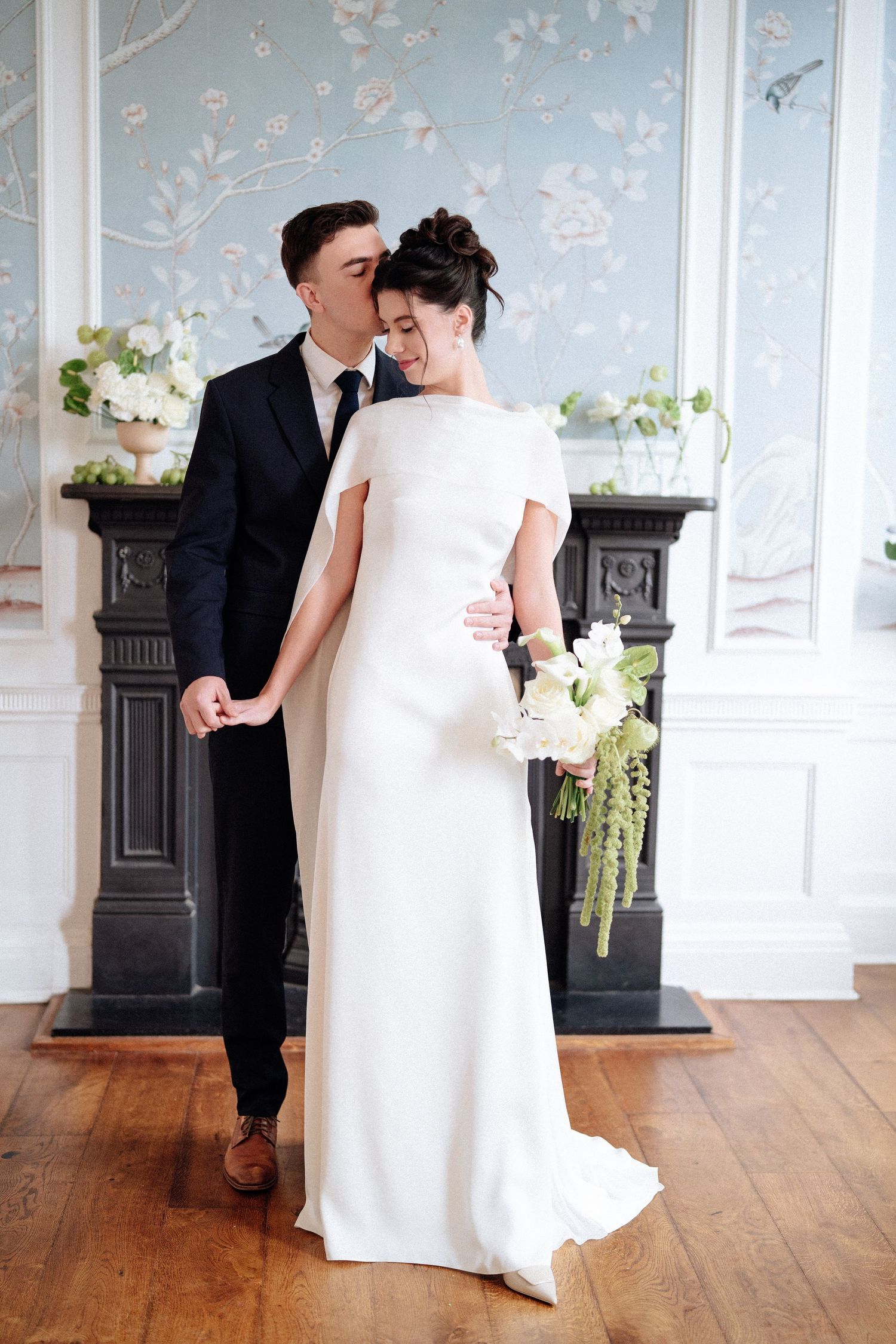 Elegant couple dancing in a beautiful room with blue floral wallpaper and hardwood floors.