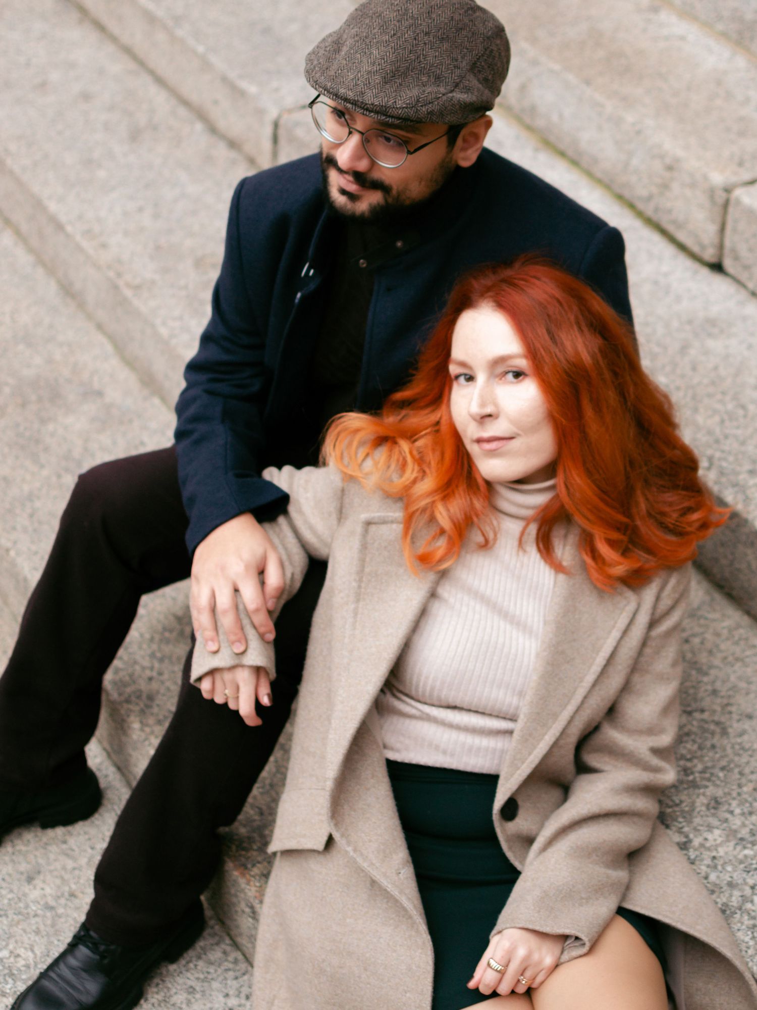 Couple in vintage-inspired outfits sitting close together on concrete steps.