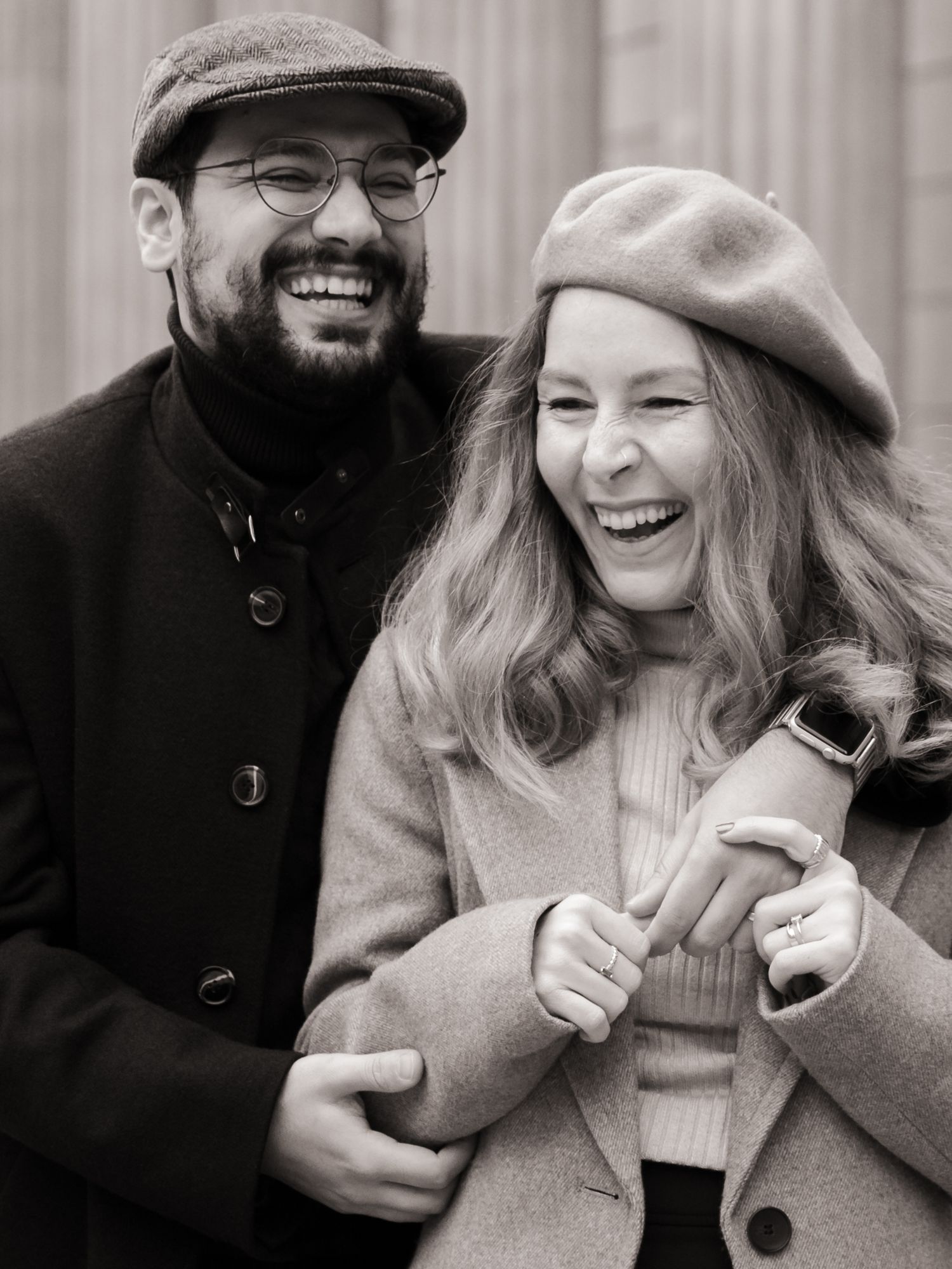 Candid black and white photo of a laughing couple in winter coats.