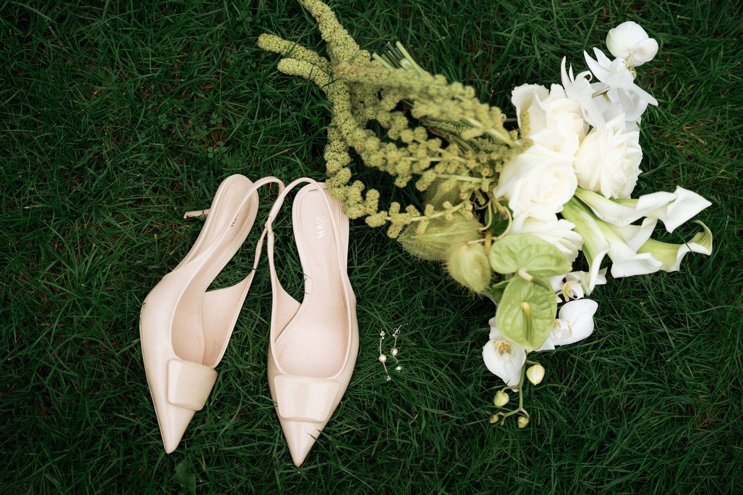 White orchids and delicate pink high heel shoes arranged on lush green grass create an elegant bridal composition.