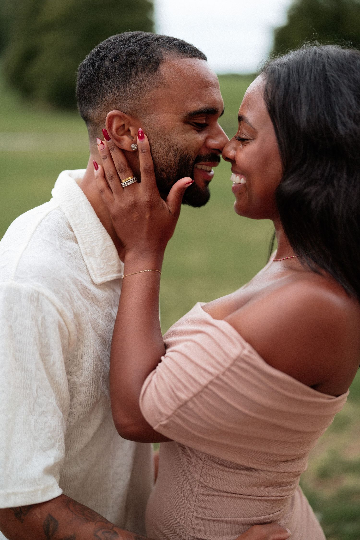 A joyful couple shares a tender moment outdoors, with her hand on his cheek.