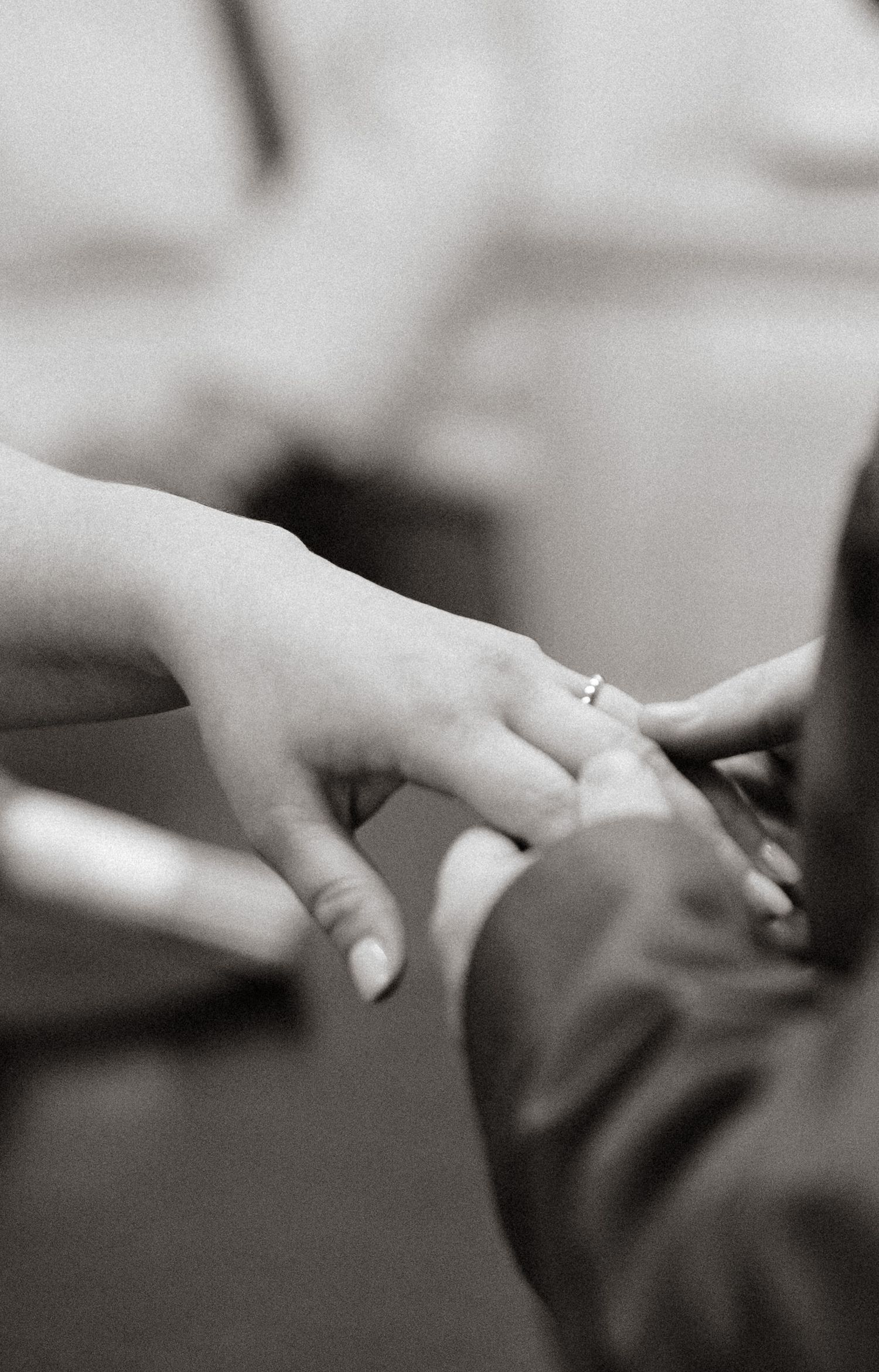 A close-up black and white photo of hands exchanging rings during a wedding ceremony.