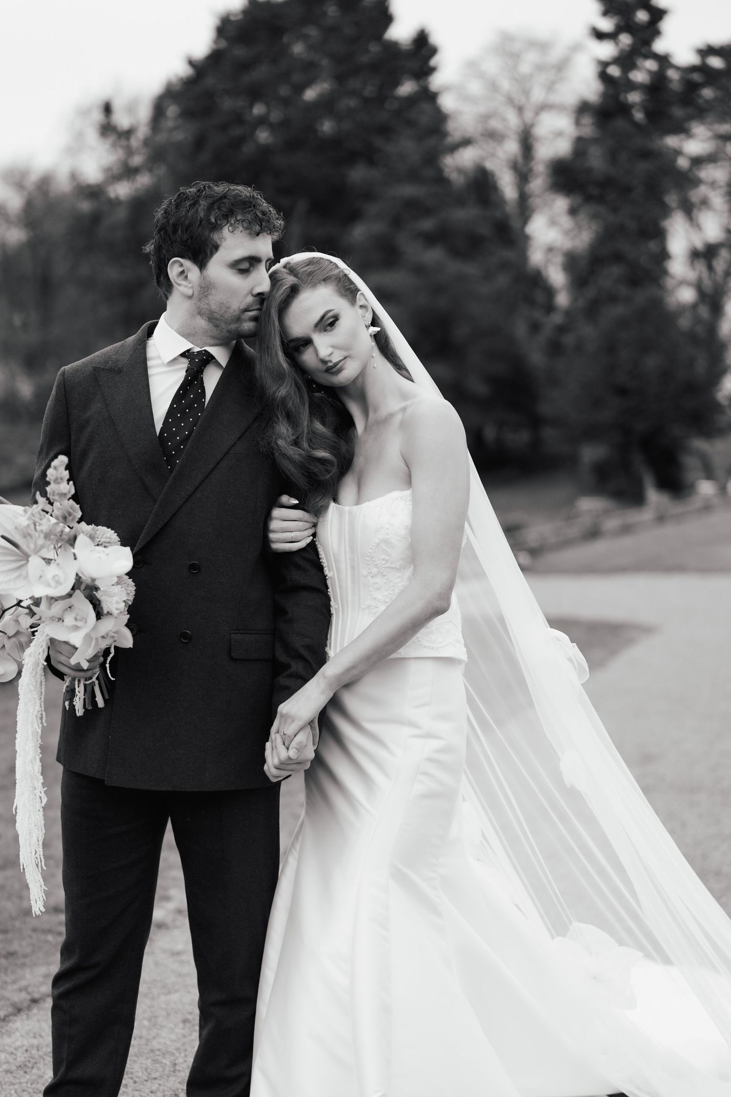 Black and white wedding portraits of a couple embracing outdoors with the bride's veil flowing in the wind.