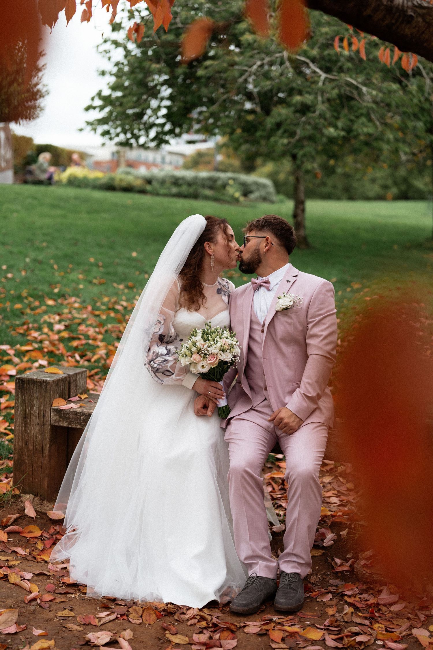 Romantic autumn wedding photos with couple sitting on log surrounded by fallen leaves.