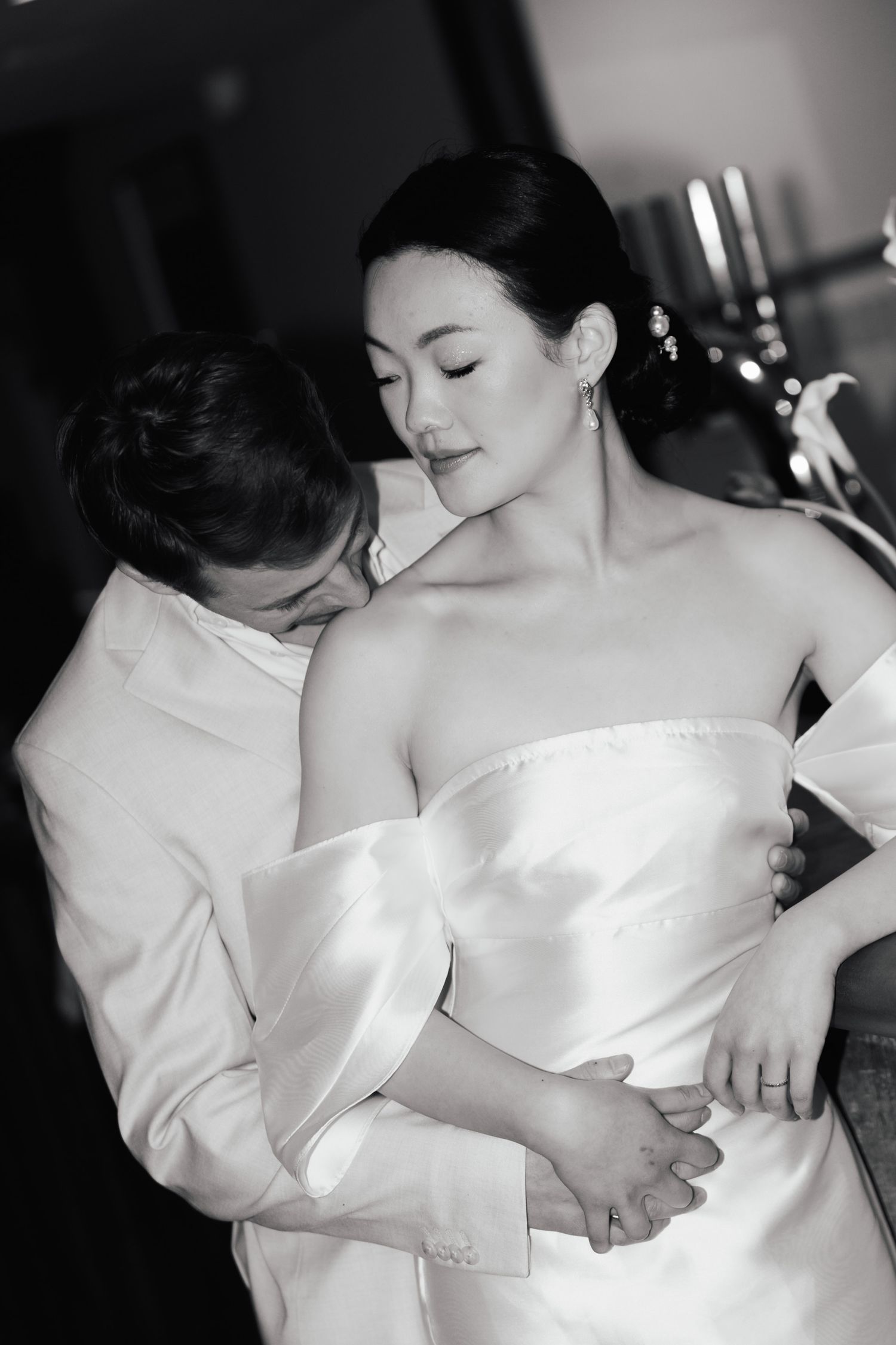 Black and white wedding photo of groom embracing bride in strapless gown, sharing an intimate moment.