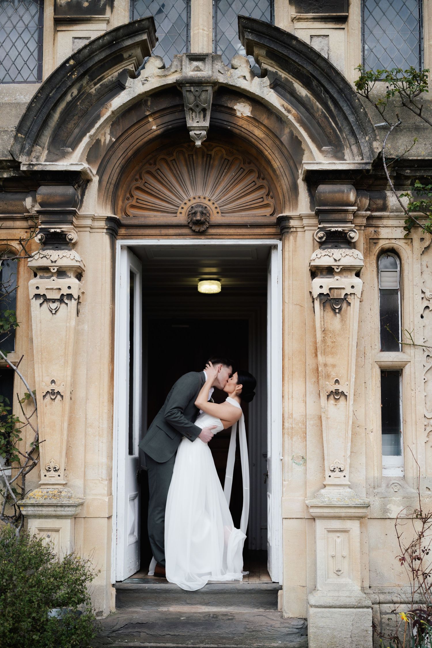 Bride and groom share a romantic dip kiss in an ornate stone doorway of a historic wedding venue.