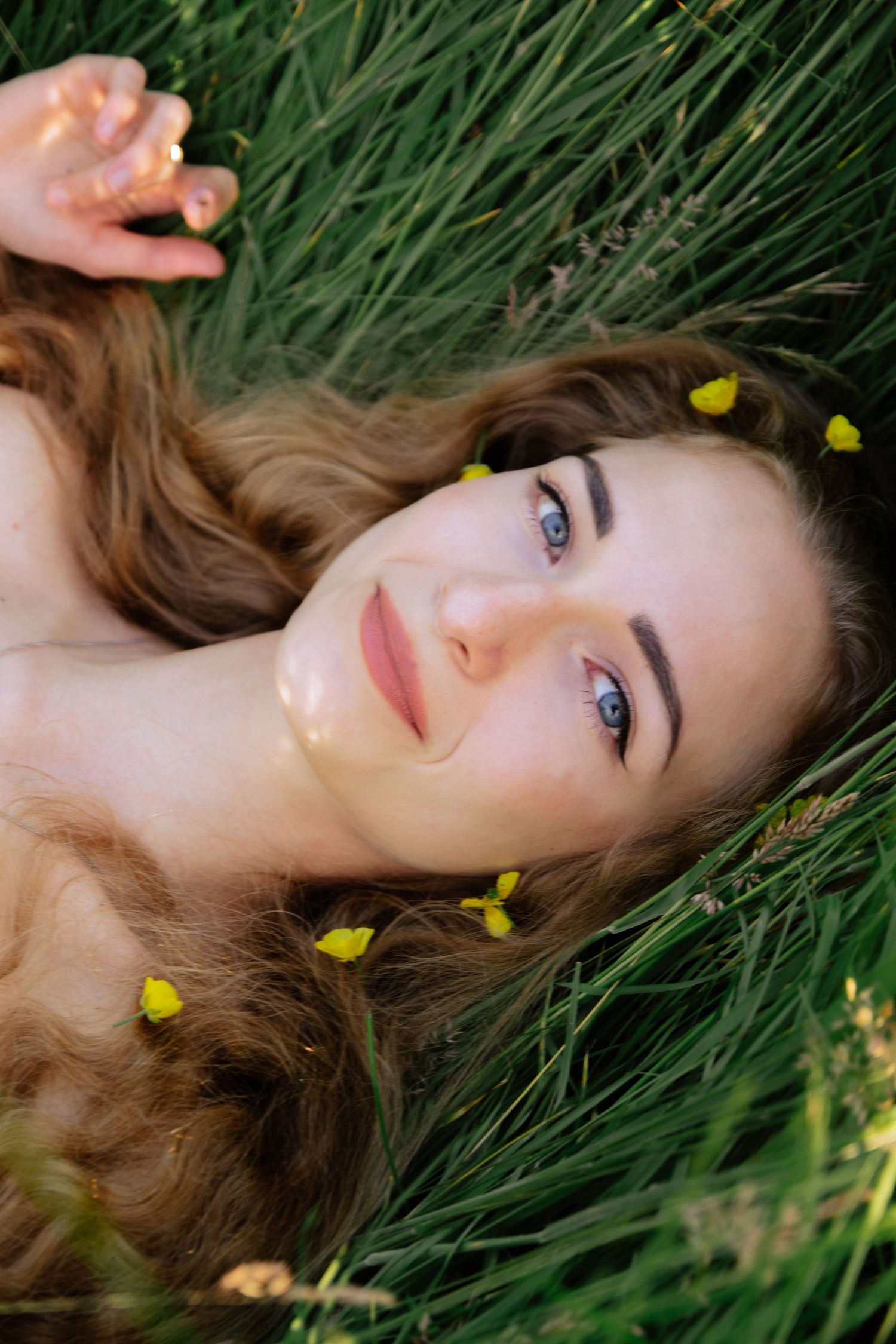 Portrait of woman lying in tall grass with yellow flowers scattered around her hair.