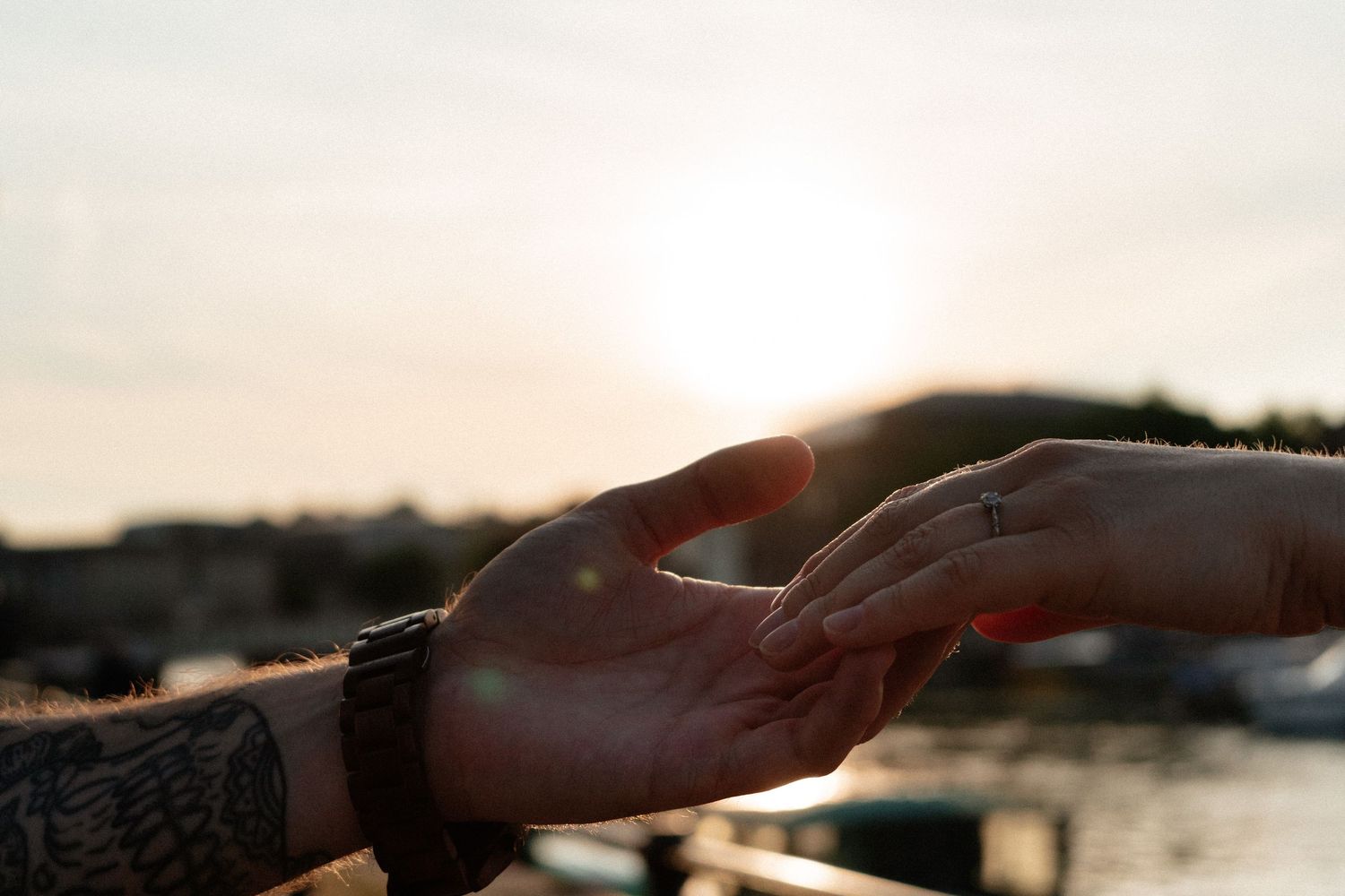 Silhouetted hands reaching across a sunset sky over water.