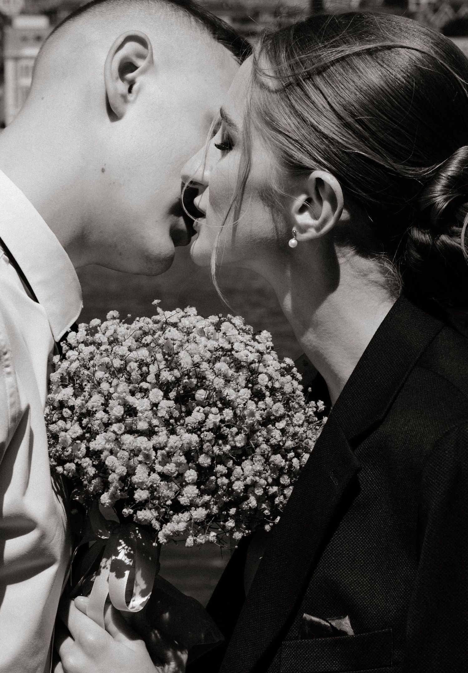 Black and white photo of a couple sharing a romantic kiss while holding a bouquet of baby's breath flowers.