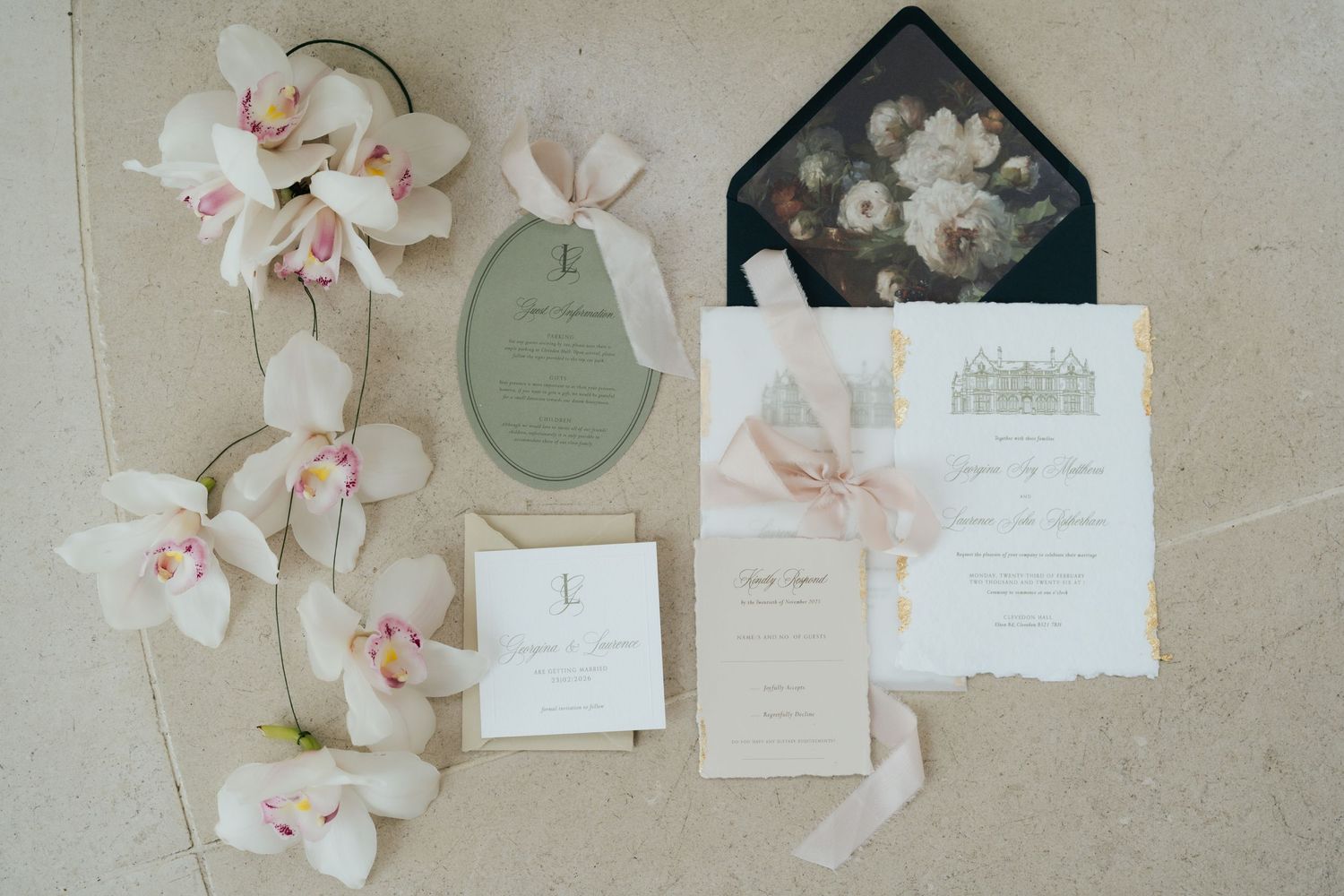 Elegant wedding invitation suite with sage green oval card, blush stationery, black floral envelope, and white orchid garland.