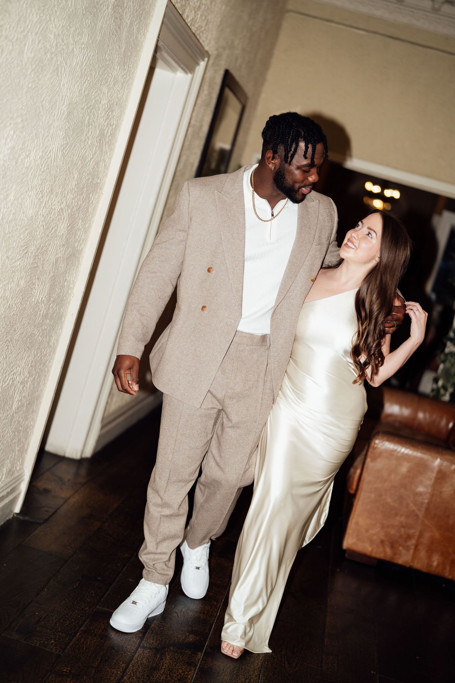 A couple in formal attire dancing together in an indoor venue with hardwood floors and white walls.